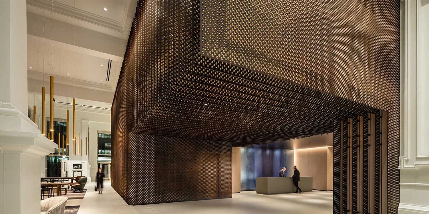 Modern interior atrium with dramatic bronze mesh ceiling canopy, warm ambient lighting, and minimalist dark wood accents by Ferra Designs.