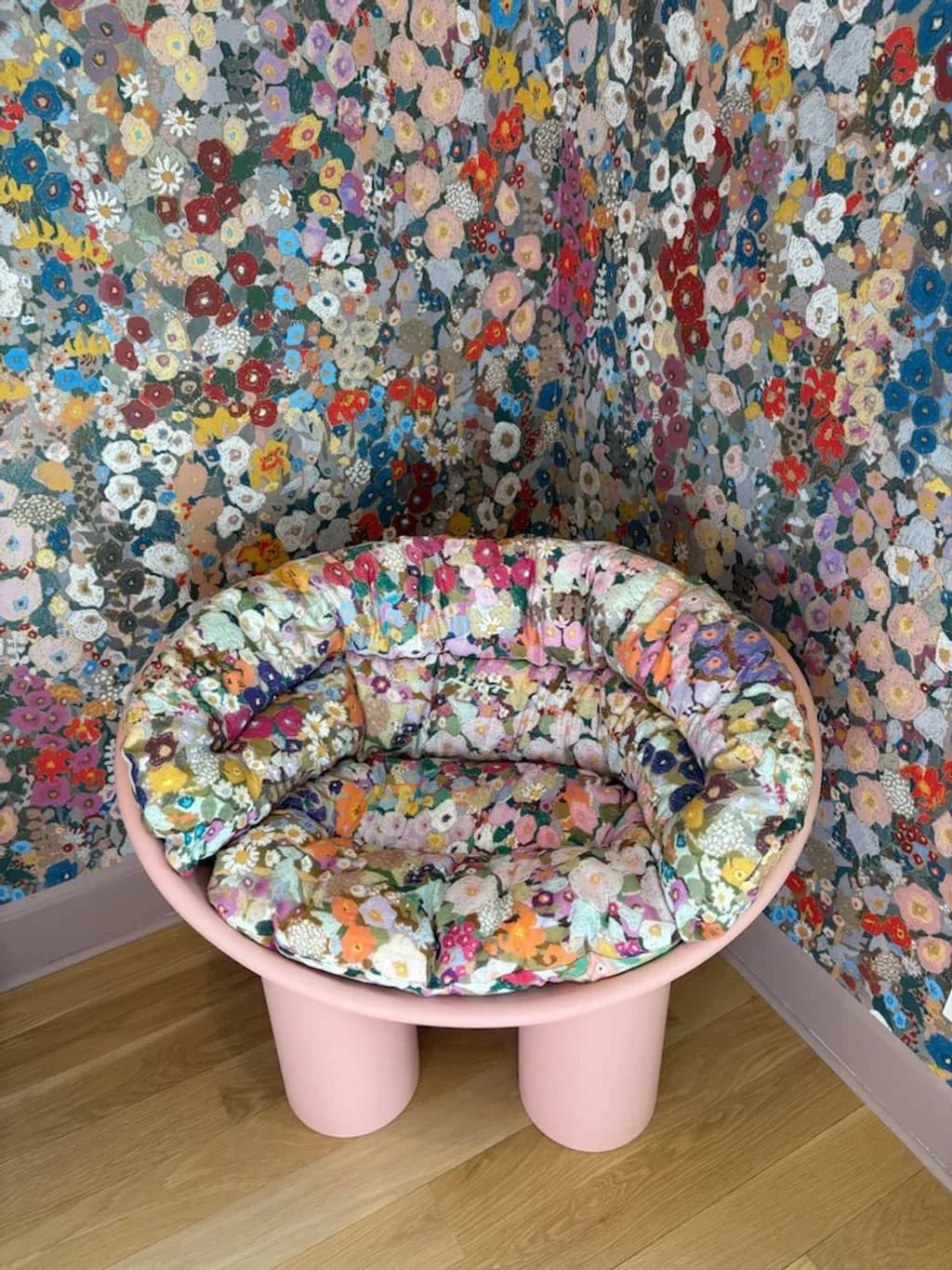 Pink upholstered chair with floral patterned seat cushion positioned in a corner room with matching colorful floral wallpaper by Find the Thread Upholstery.