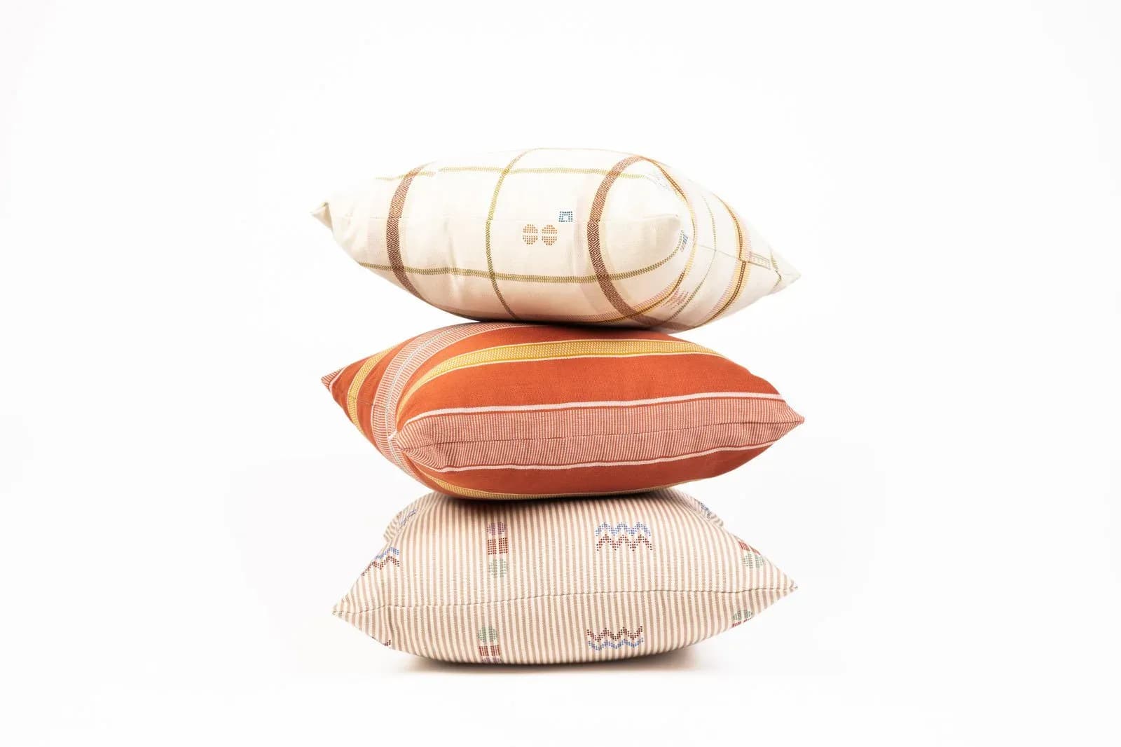 Stacked upholstered pillows in cream, coral, and striped fabrics with a cylindrical bolster on top, showcasing textile design work by Find the Thread Upholstery.