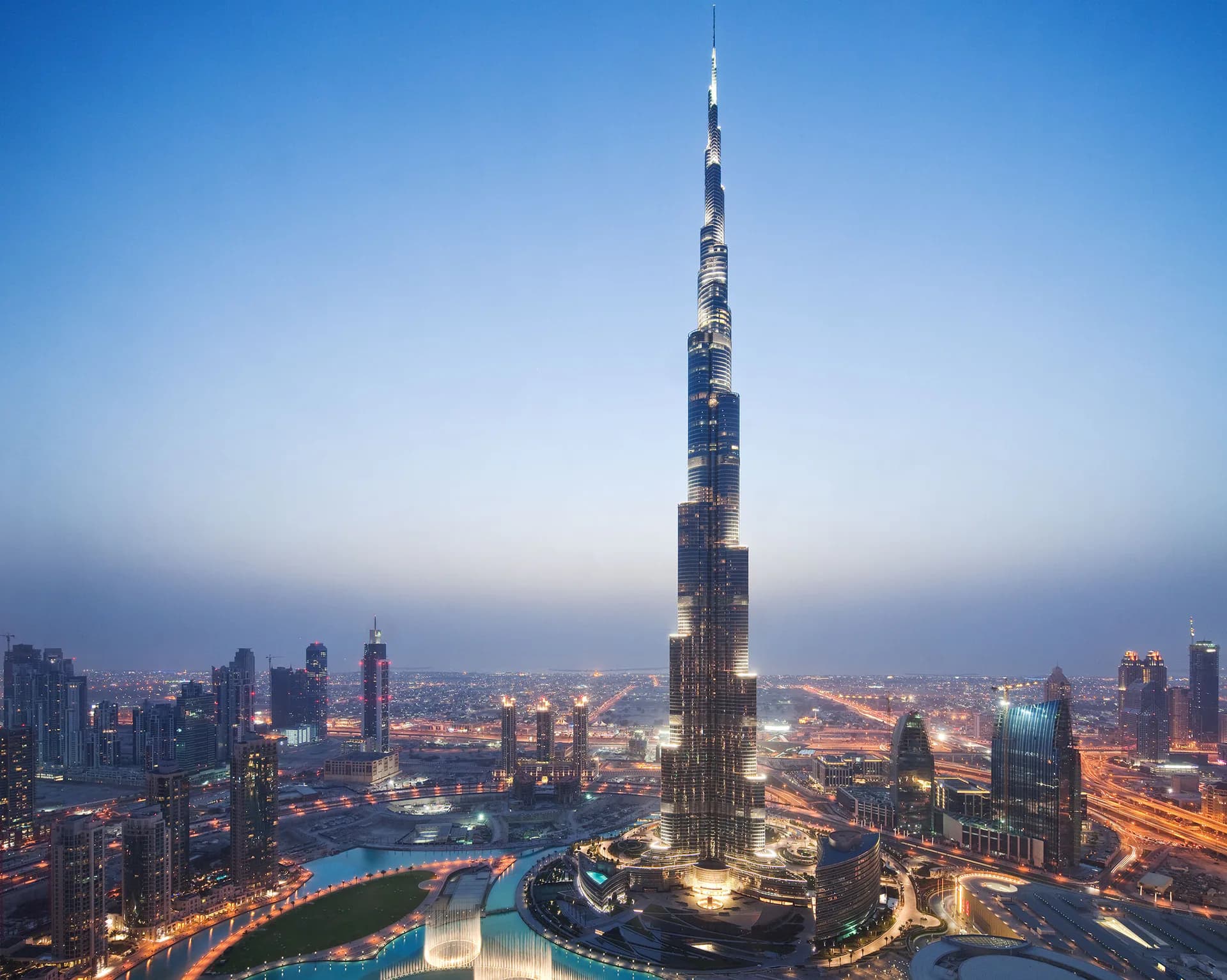 Burj Khalifa illuminated at dusk with surrounding Dubai cityscape and curved waterway, architectural photography by Fisher Marantz Stone.