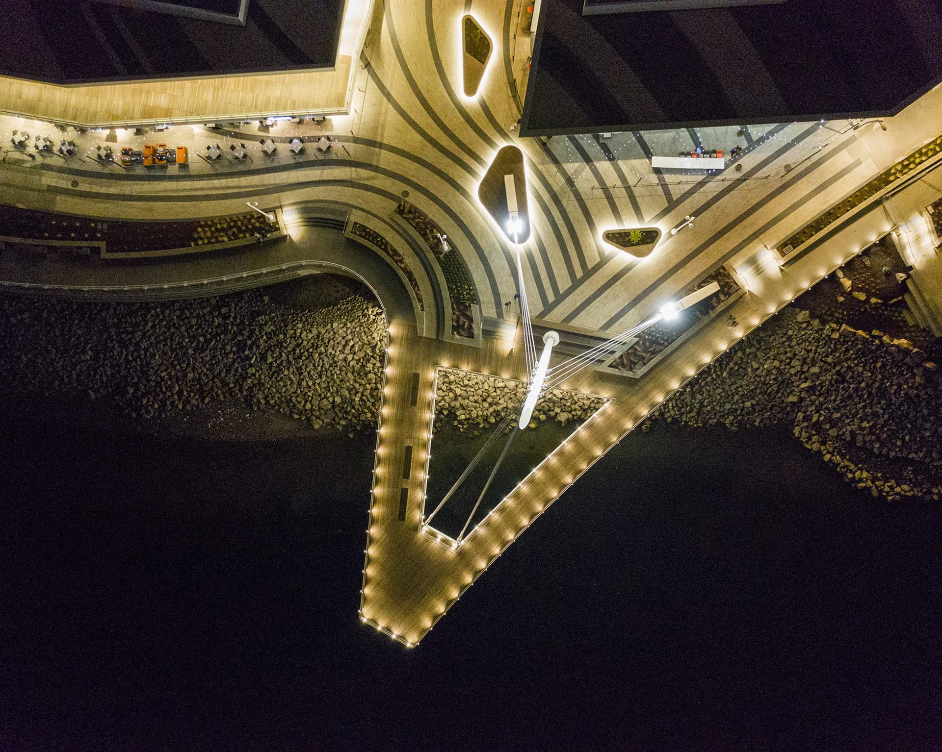 Aerial nighttime view of illuminated curved architectural structure with warm LED lighting along edges and geometric cutout details, by Fisher Marantz Stone.