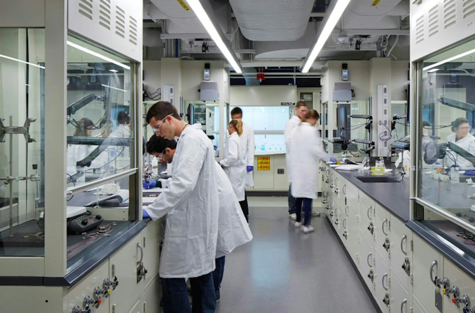 Modern laboratory interior with glass-fronted workstations, white cabinetry, and bright LED ceiling panels, designed by Flad Architects.