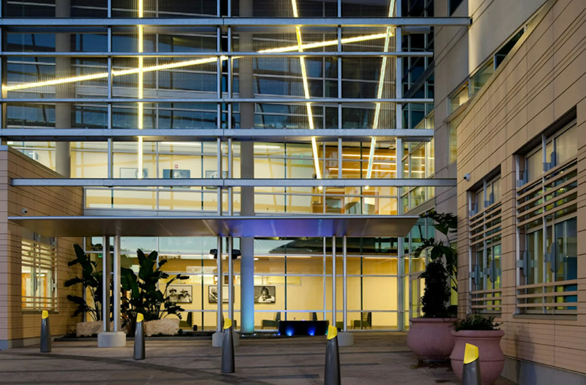 Modern glass-fronted building entrance with warm wood cladding, illuminated interior spaces, and planted courtyard area by Flad Architects.