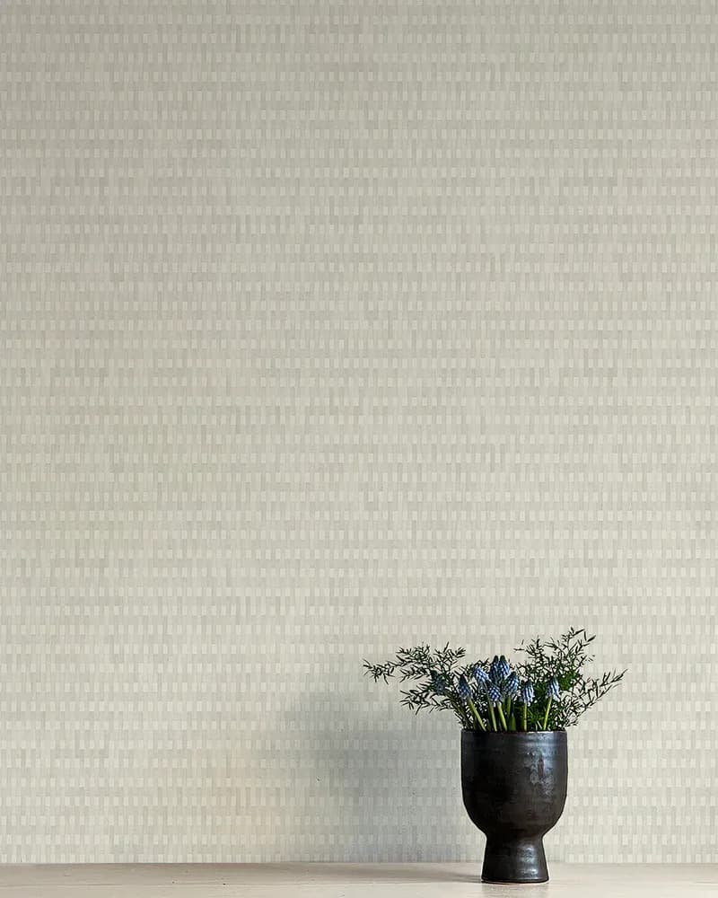 Minimalist interior with textured cream wallpaper, black sculptural vase holding blue flowers and greenery by Flat Vernacular.