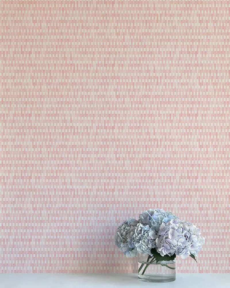 Minimalist interior with soft pink geometric wallpaper and white shelf displaying blue hydrangeas in glass vase by Flat Vernacular.