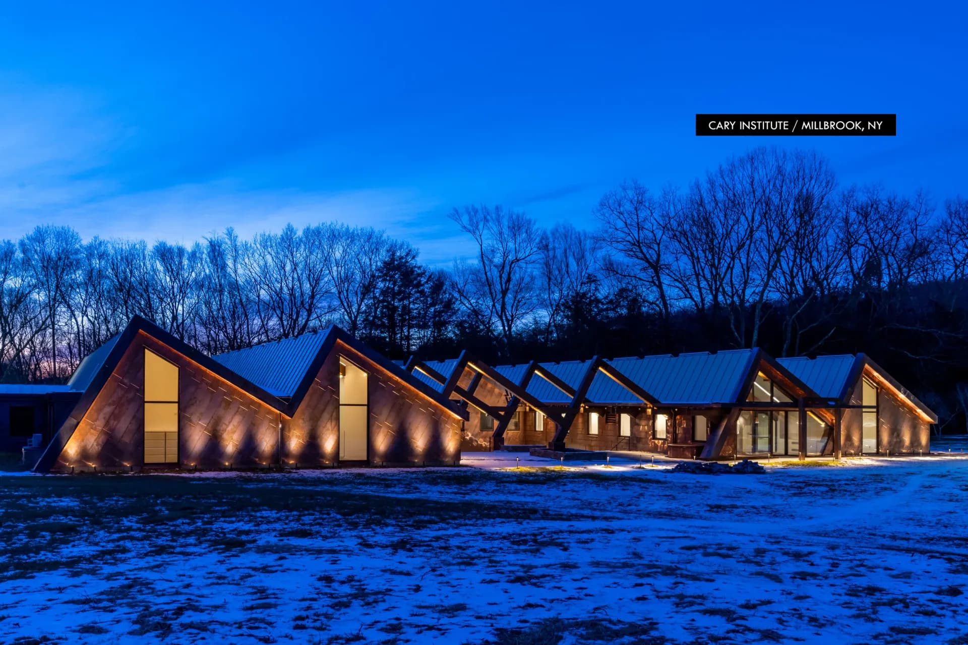 Modern angular building with illuminated windows set against snowy landscape at dusk, designed by Focus Lighting.