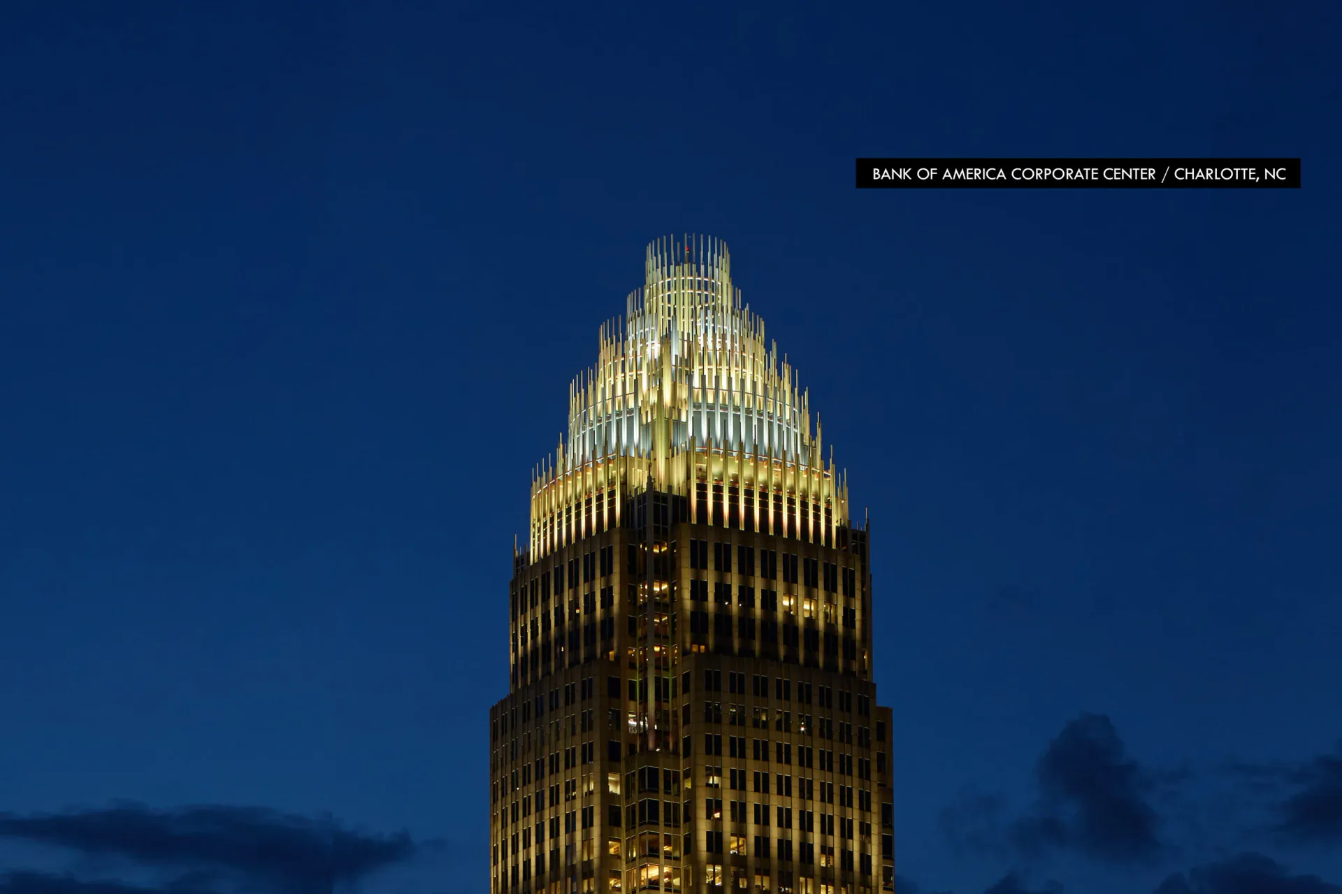 Bank of America Corporate Center tower illuminated at dusk with golden uplighting against deep blue sky, designed by Focus Lighting.