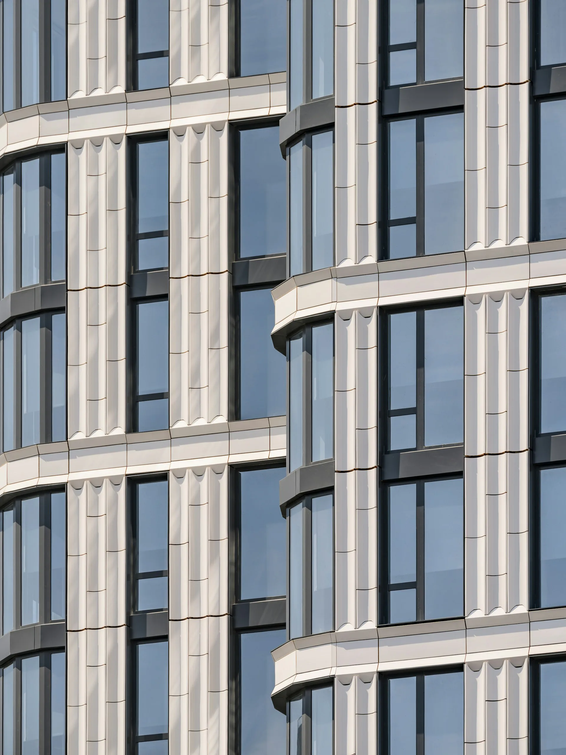 Curved façade of a residential building with cream-colored stone cladding, tall vertical windows, and rounded bay projections by Fogarty Finger.
