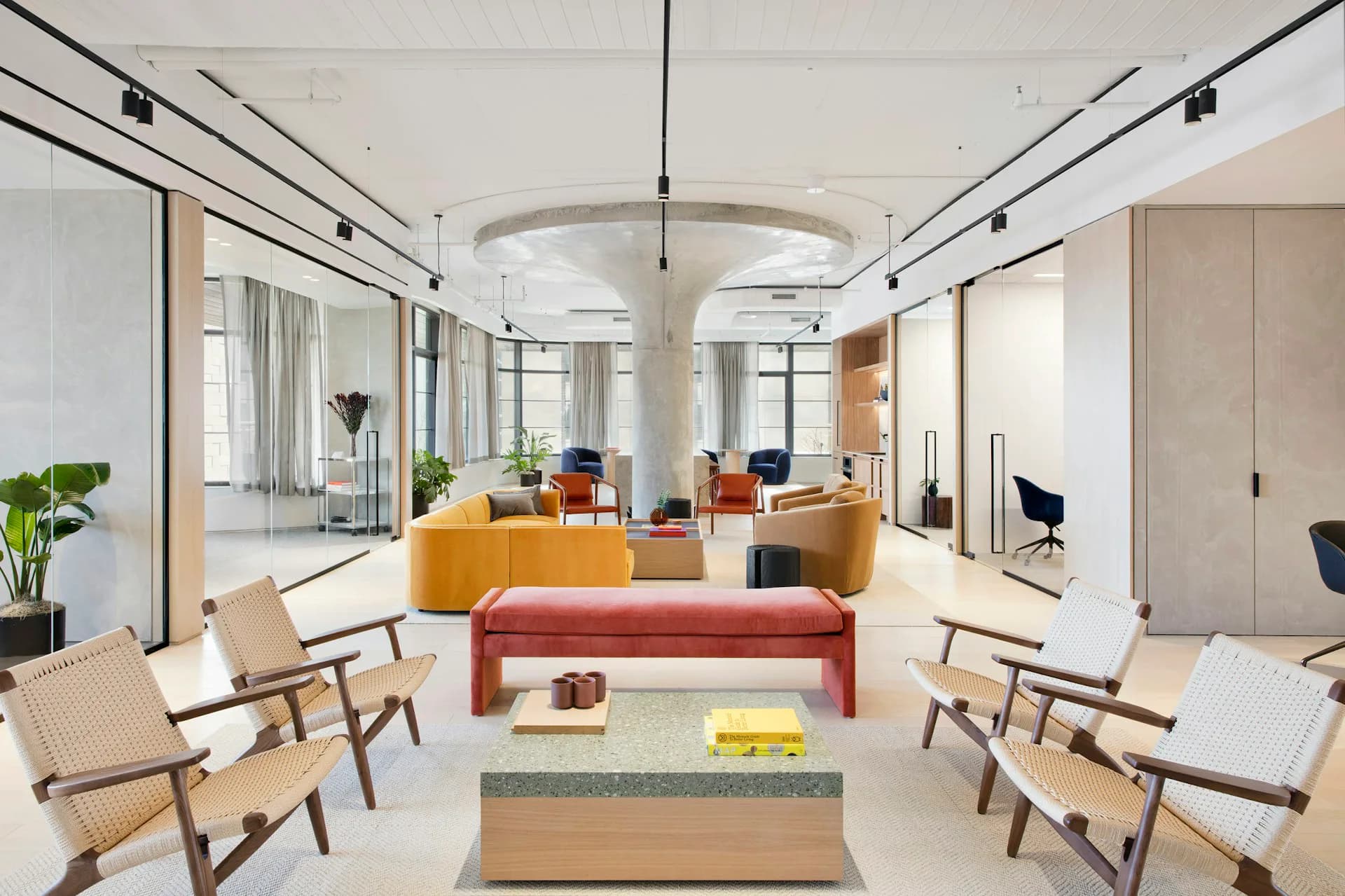 Bright modern office lounge featuring yellow and red seating, natural wood chairs, cylindrical column, and floor-to-ceiling glass partitions by Fogarty Finger.