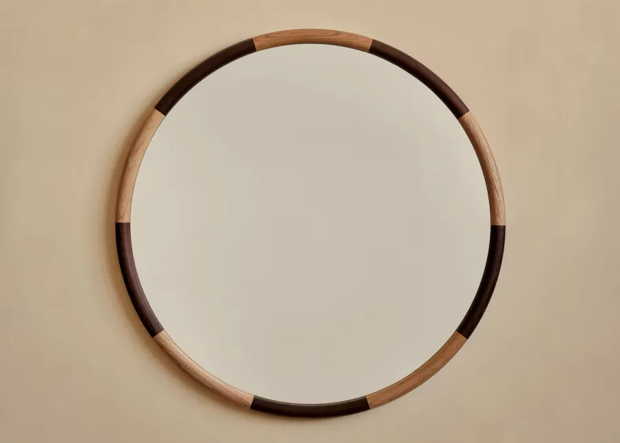 Circular wooden mirror with alternating dark and natural wood segments mounted on a neutral wall by Fort Standard.
