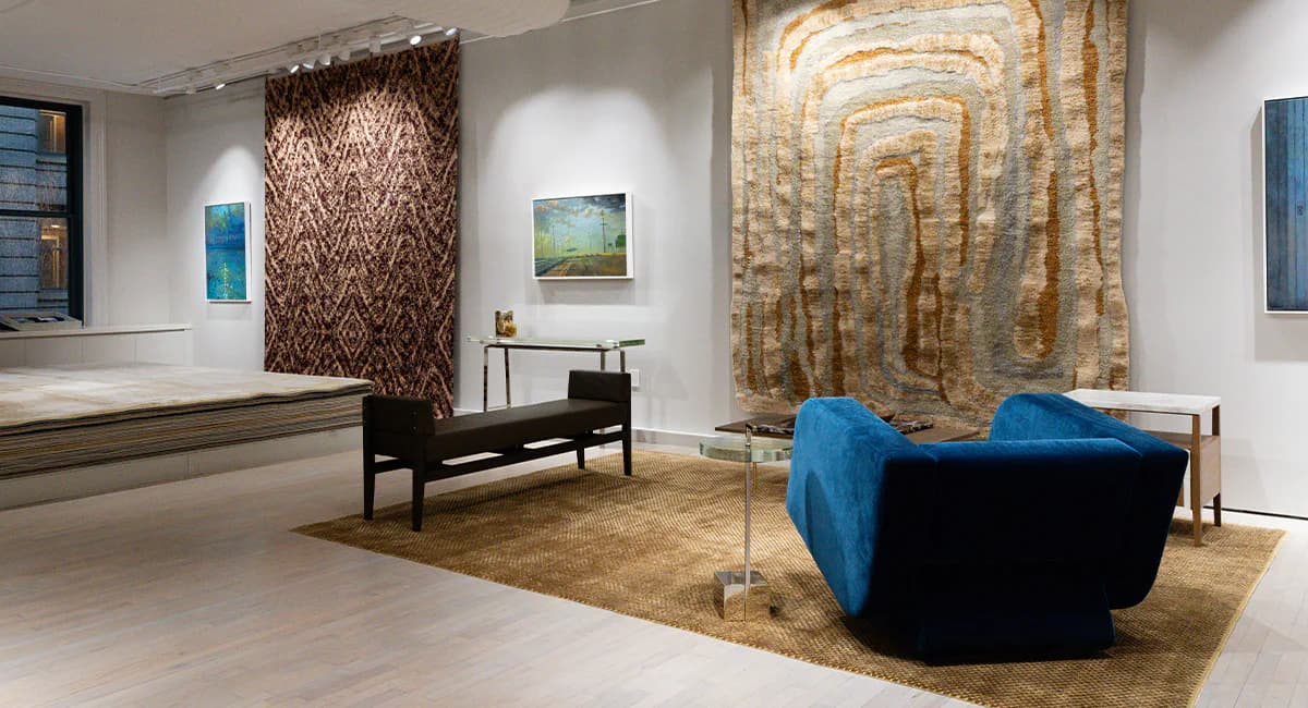 Contemporary gallery space featuring blue upholstered seating, abstract wall tapestries in earth tones, and minimal furnishings by Fort Street Studio.