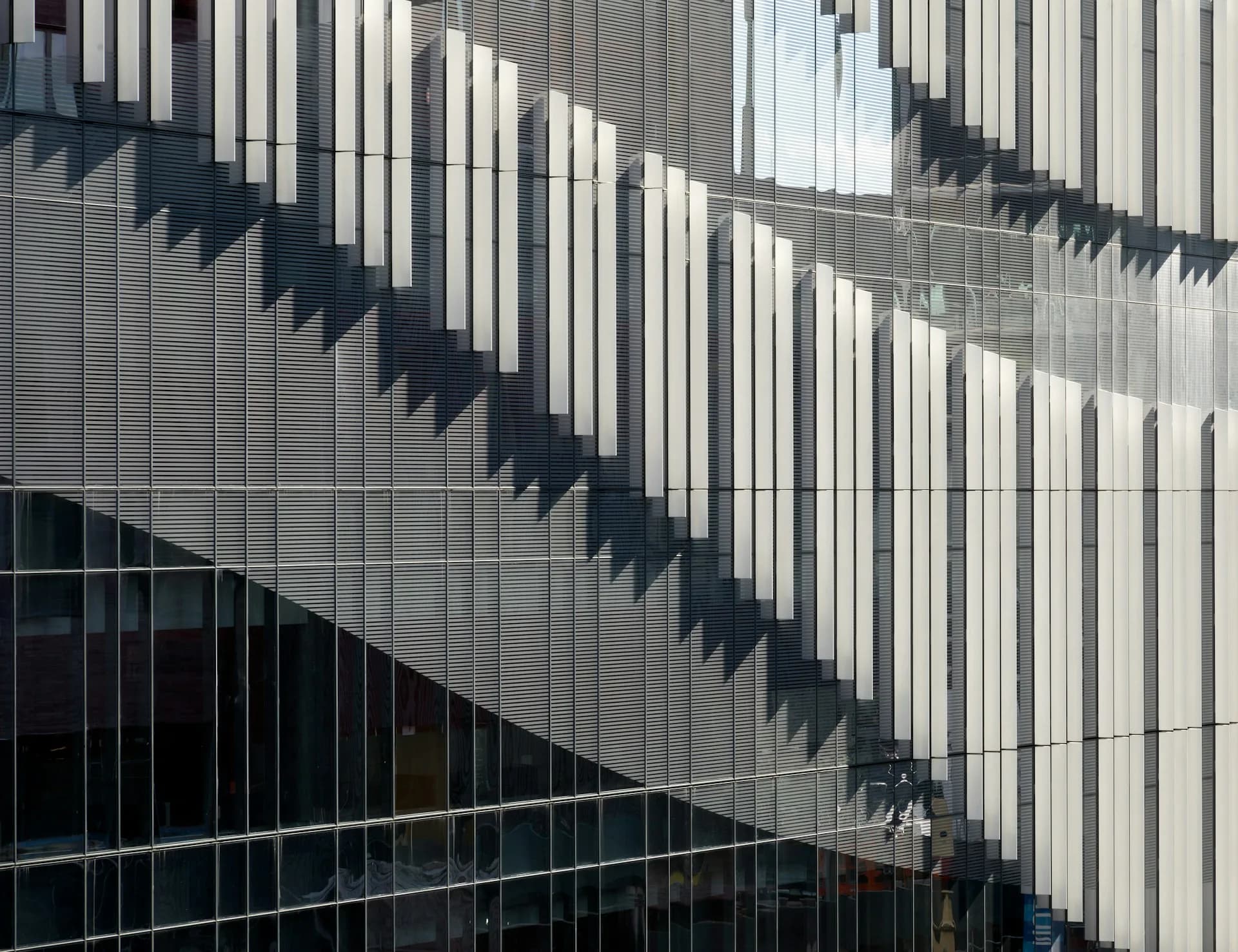 Modern building facade with vertical metal louvers casting dramatic diagonal shadows across white and dark paneled surfaces, architectural photography by Francis Cauffman.