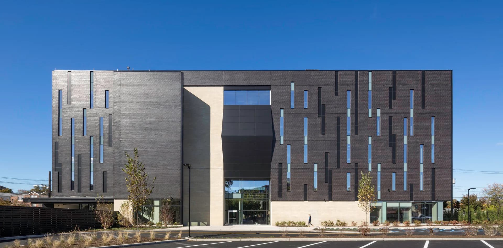 Modern multi-story institutional building with concrete and dark metal facade featuring vertical window patterns and contemporary landscaping by Francis Cauffman.