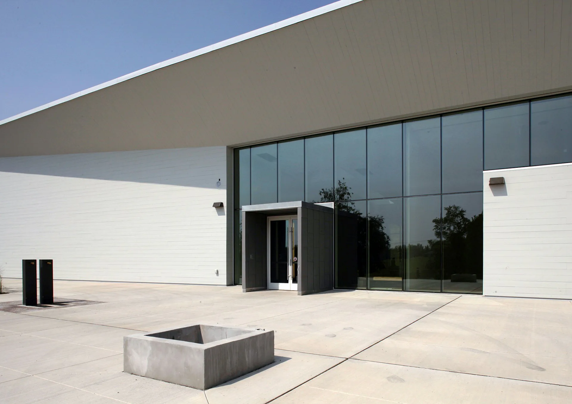 Modern institutional building with minimalist aesthetic featuring white walls, large glazed curtain wall, concrete courtyard with sunken planter by Francois de Menil Architect, PC.