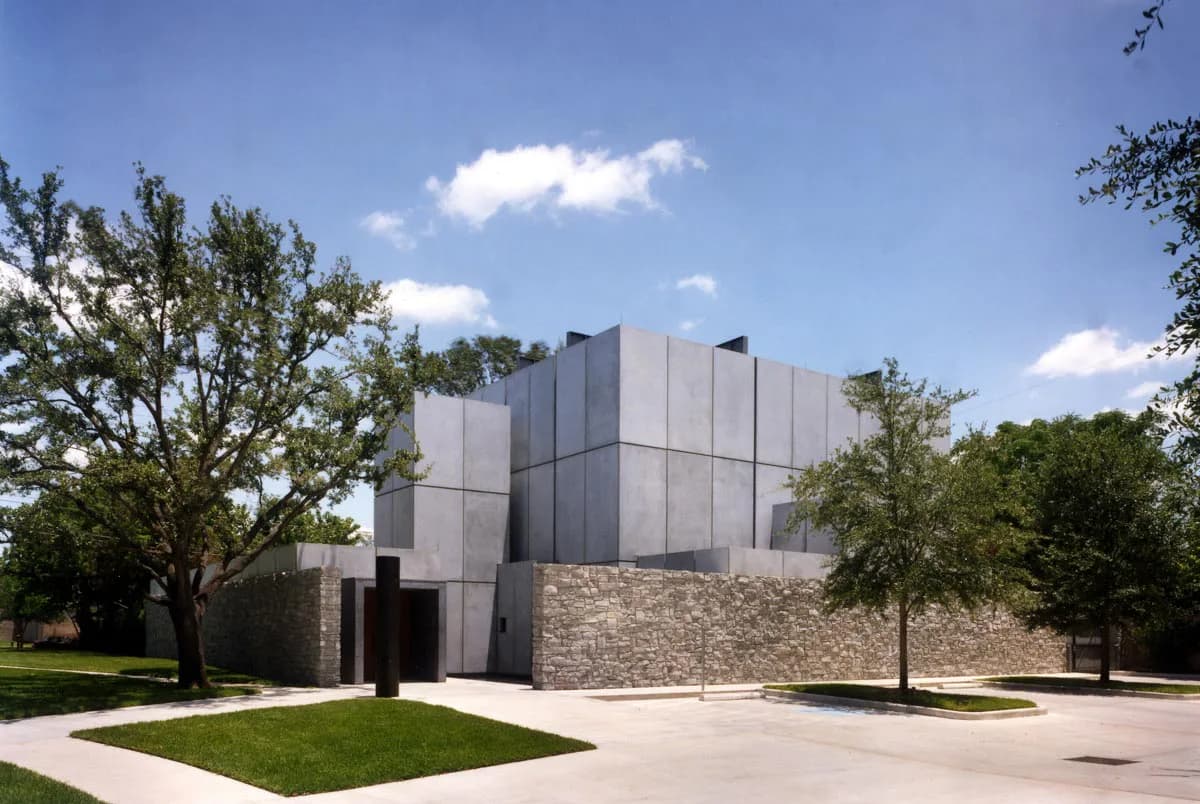 Modern institutional building with metal-clad upper volume and stone base, surrounded by mature trees and manicured lawn, by Francois de Menil Architect, PC.