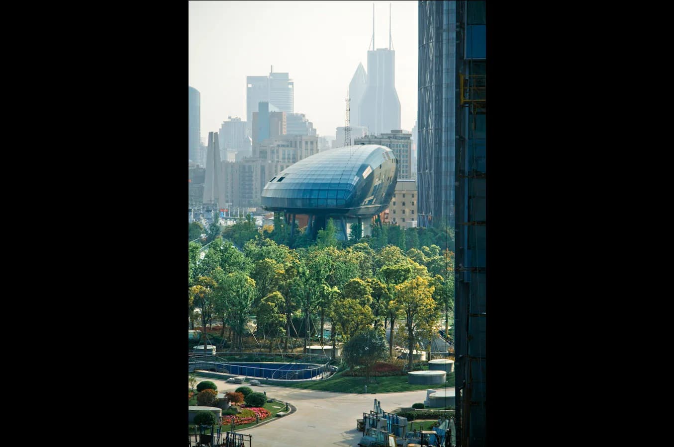 Futuristic blue airship hovering above a sunlit urban park with trees, backed by a dense Manhattan skyline of tall buildings by Frank Repas Architecture.