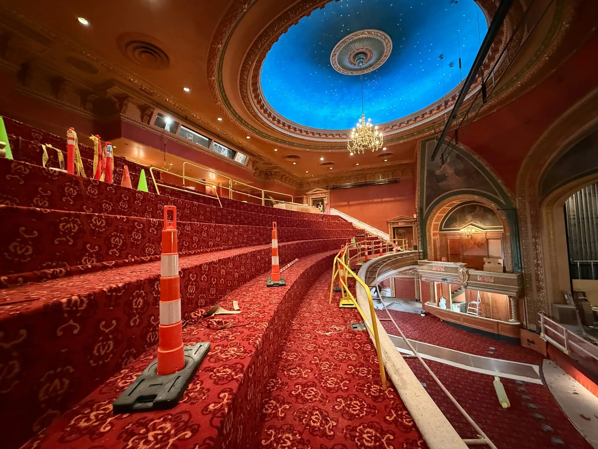 Historic theater interior with curved red velvet seating, ornate ceiling dome with blue skylight, and decorative architectural details by Fred Basch Architect PLLC.