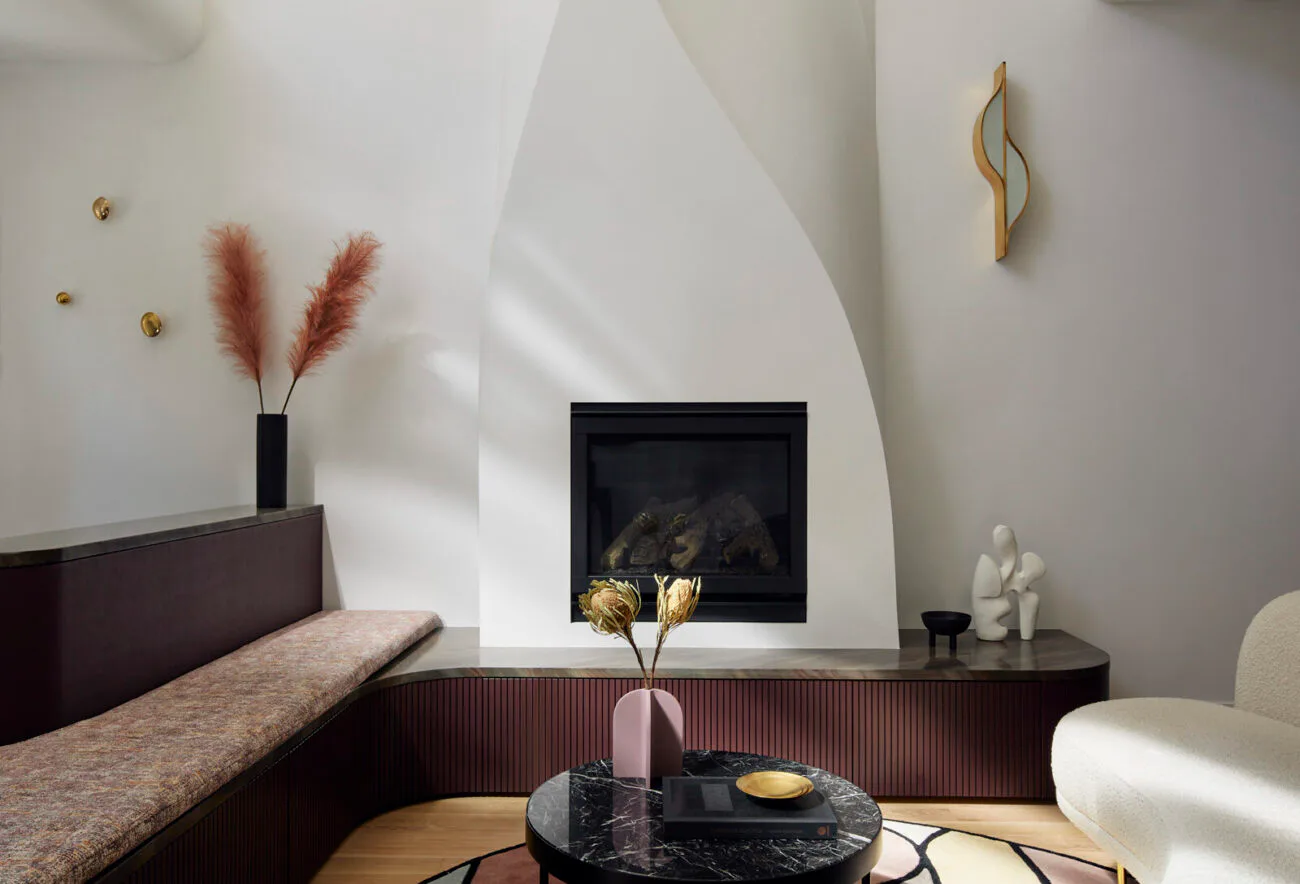 Modern bedroom with curved white wall, dark wood headboard, black fireplace, potted pampas grass, and minimalist furnishings by Frederick Tang Architecture.