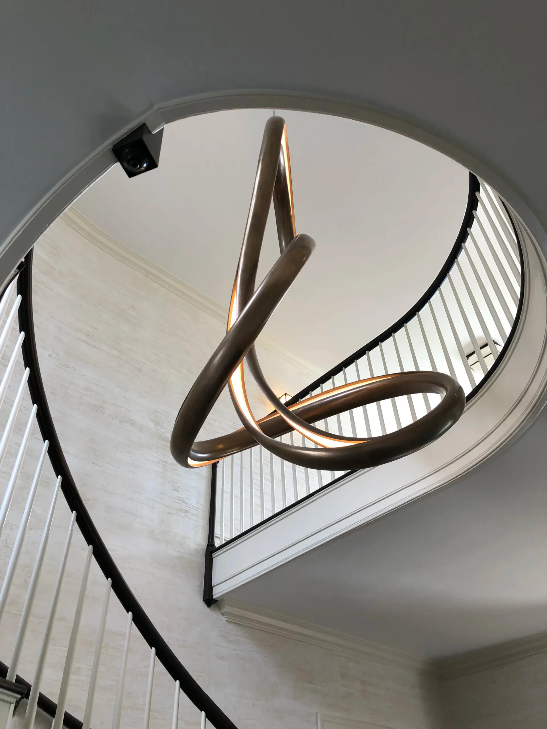 Modern spiral staircase with bronze sculptural railings, white treads, and minimalist metal detailing in a light-filled interior by Fresco Decorative Arts.