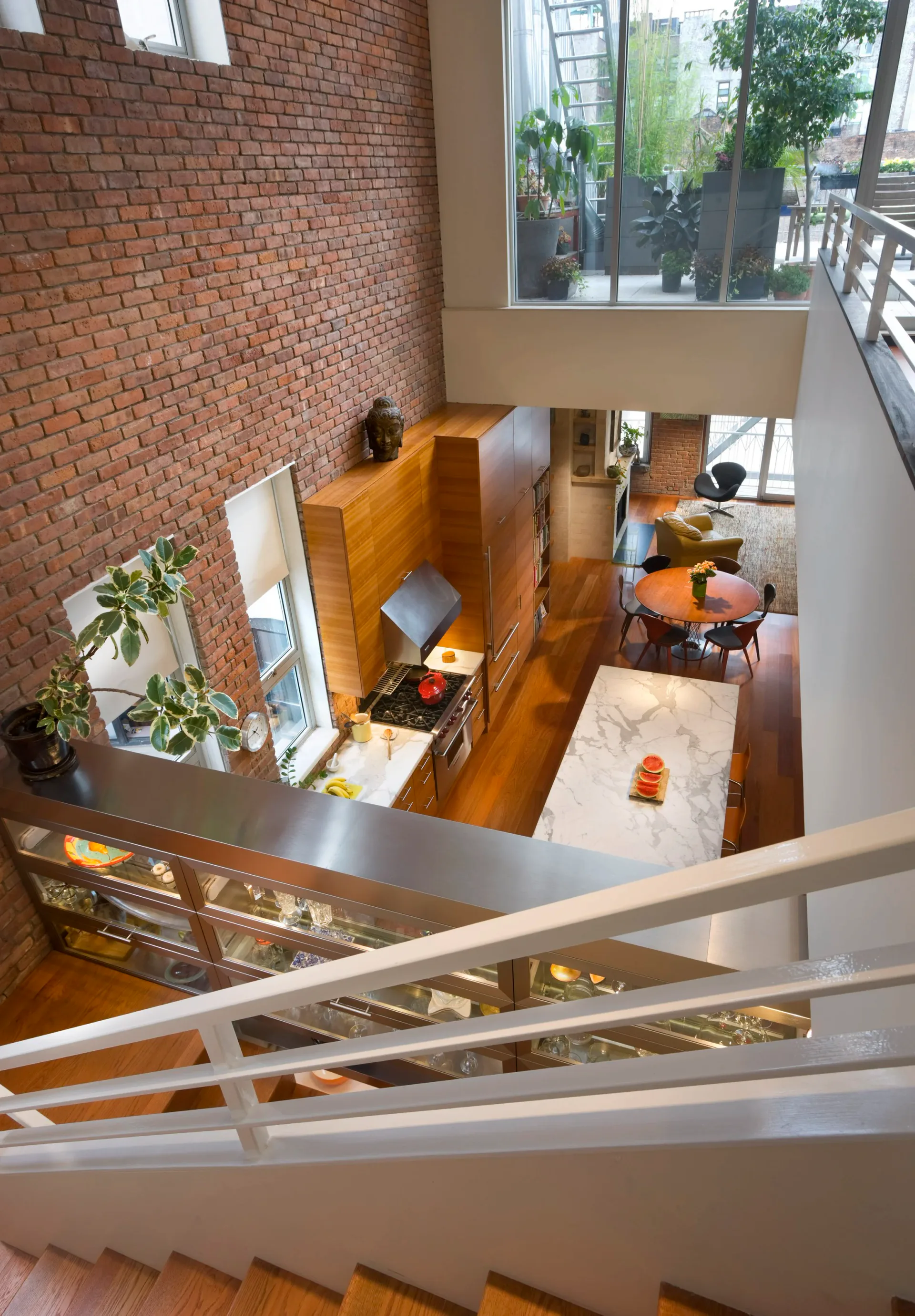 Multi-story loft interior with exposed red brick wall, wooden floors, mezzanine level, and large windows overlooking urban greenery, designed by Freyer Collaborative Architects.