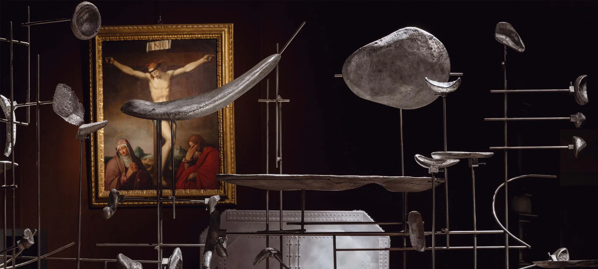 Conceptual installation merging Renaissance crucifixion painting with suspended geometric forms and scientific instruments against a dark background, by Friedman Benda.