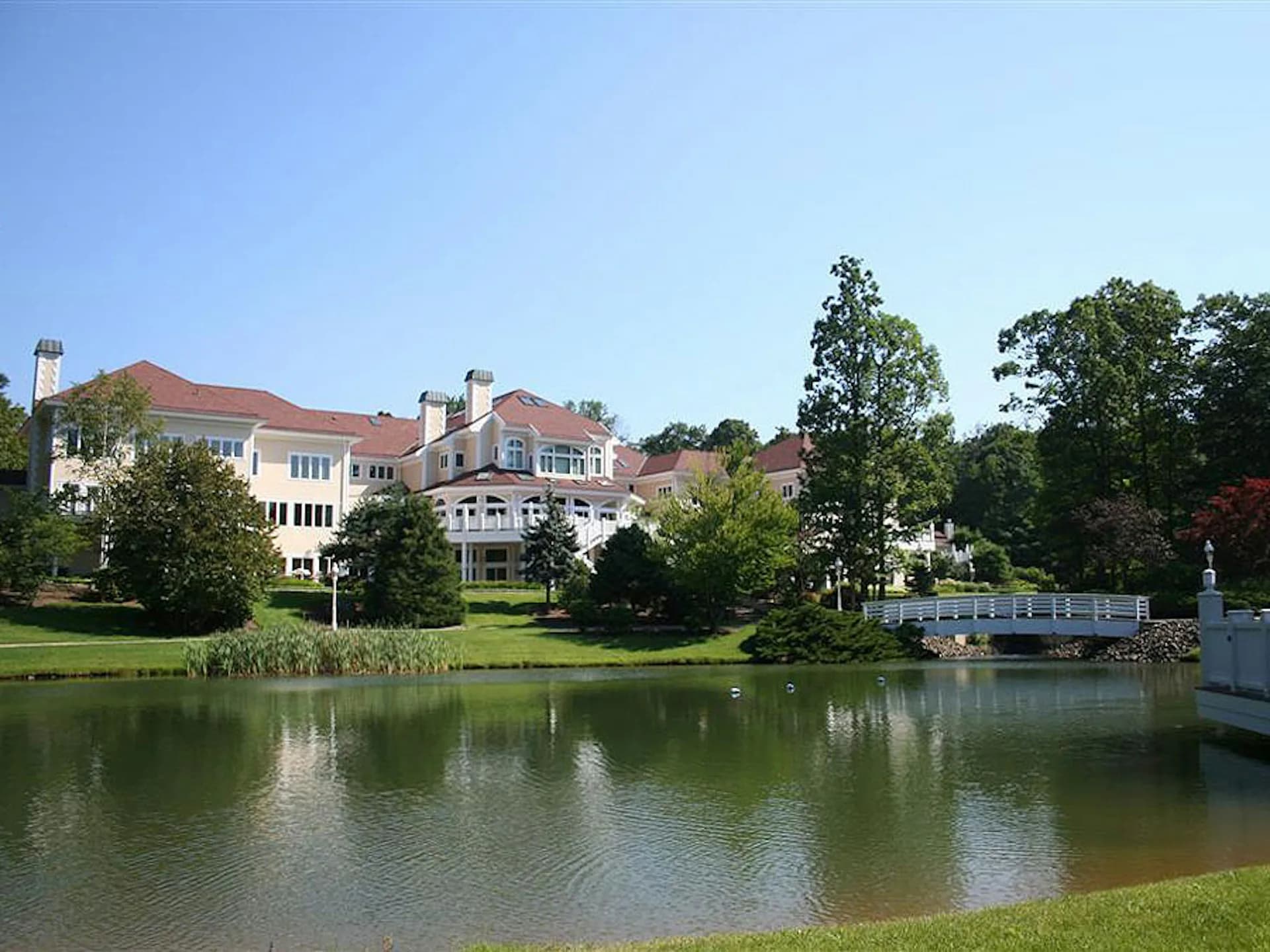 Waterfront residential estate with manicured lawns and mature trees reflected in calm water, designed by FSI Architecture PC.