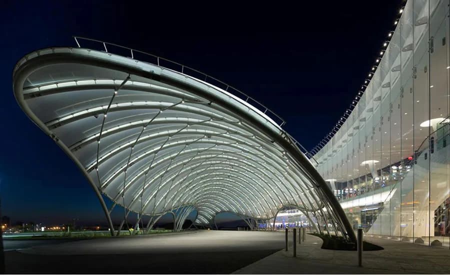 Illuminated curved tensile membrane canopy with steel ribbing spanning a modern transit plaza at night, designed by FTL DESIGN ENGINEERING STUDIO.