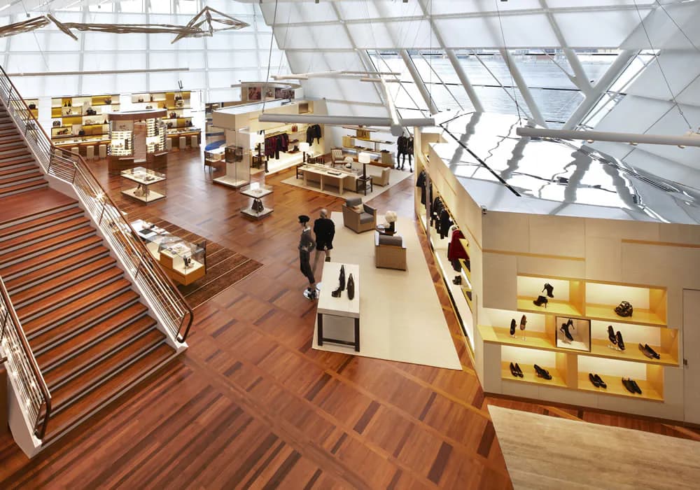 A modern retail shoe store interior with wooden flooring, illuminated display shelves, and a dramatic skylight ceiling by FTL DESIGN ENGINEERING STUDIO.