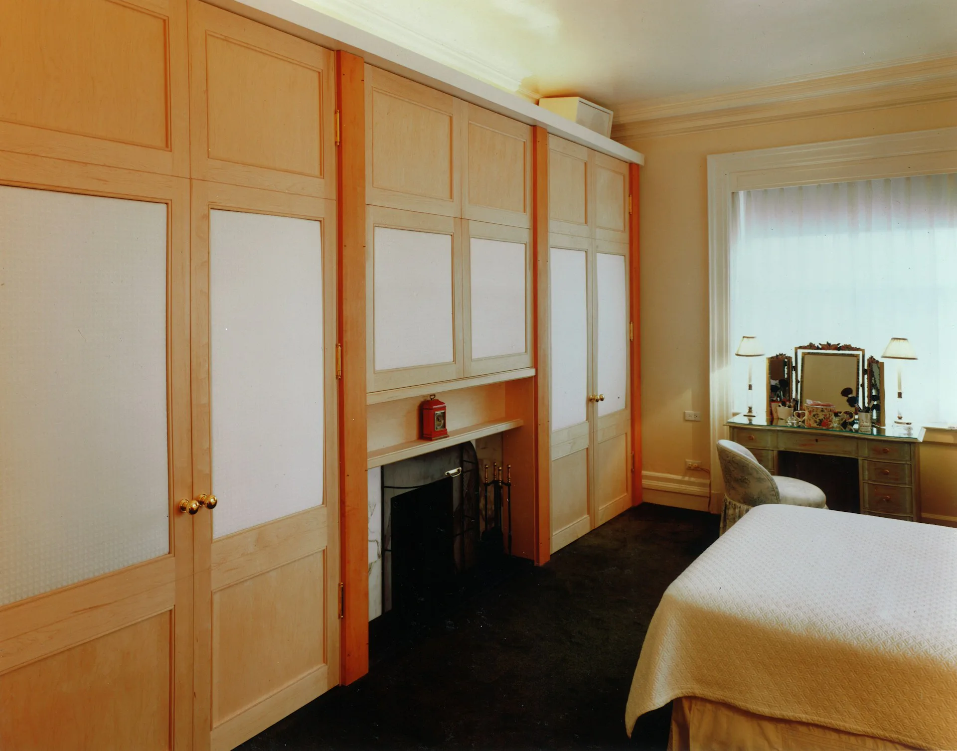 Bedroom with warm wood cabinetry, frosted glass sliding doors, black flooring, and vanity mirror in a residential interior by FZAD.