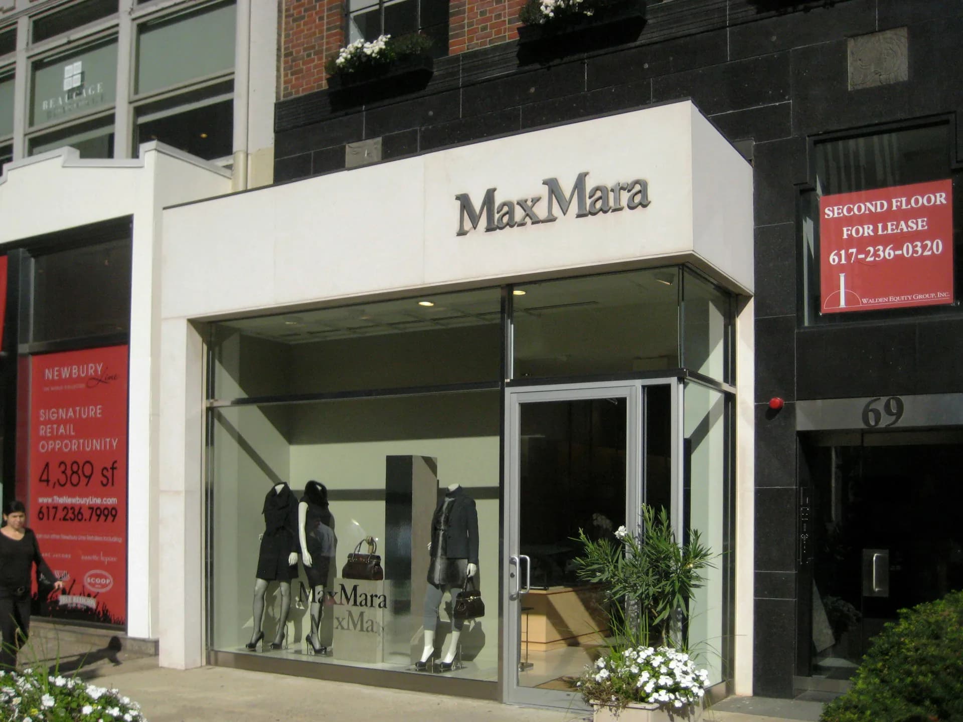 MaxMara storefront with minimalist white facade, large glass windows, and dark interior displaying fashion merchandise, designed by FZAD.