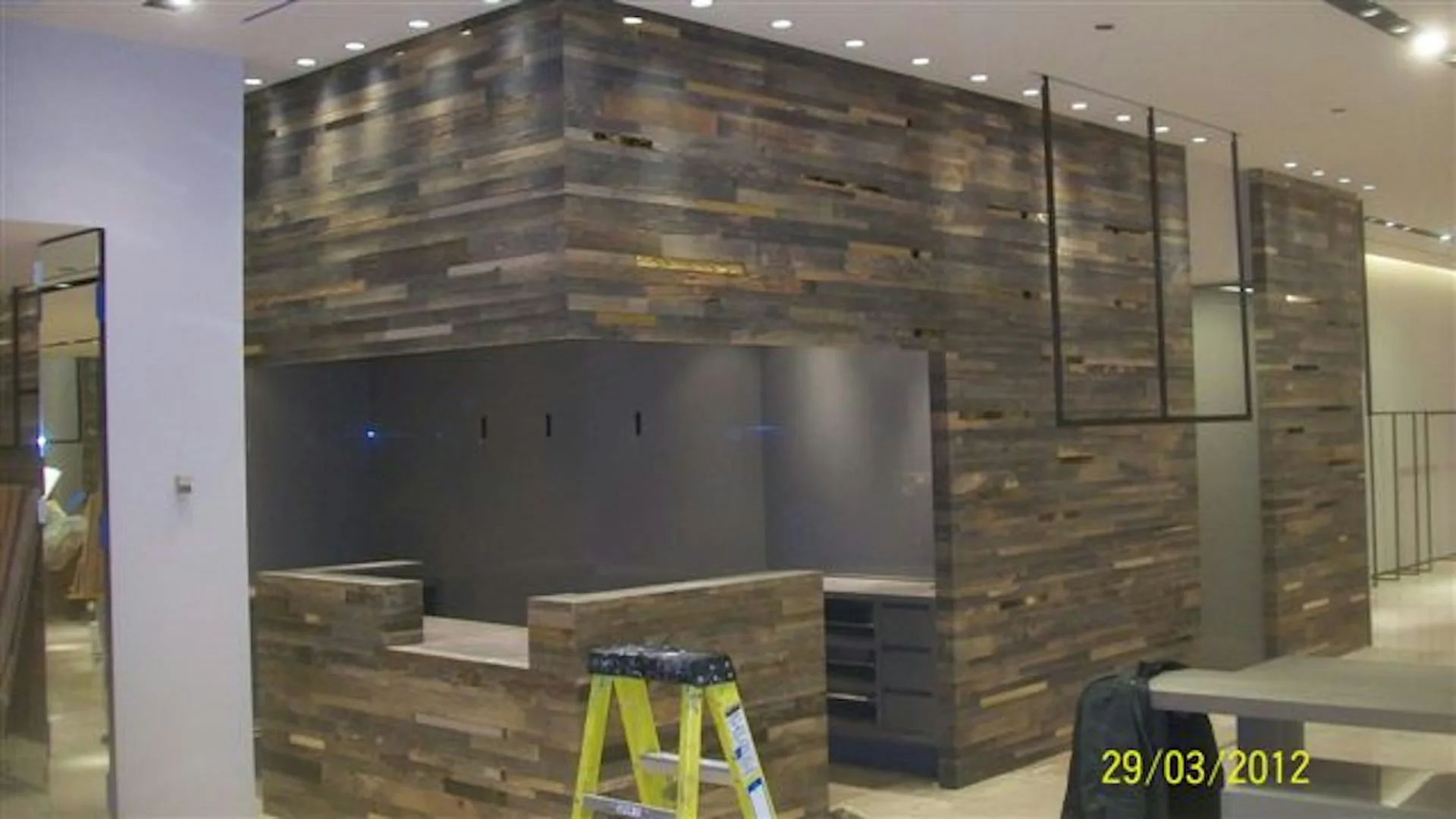 Modern interior construction showing wooden-textured wall cladding and dark interior surfaces with yellow safety equipment visible, by FZAD.