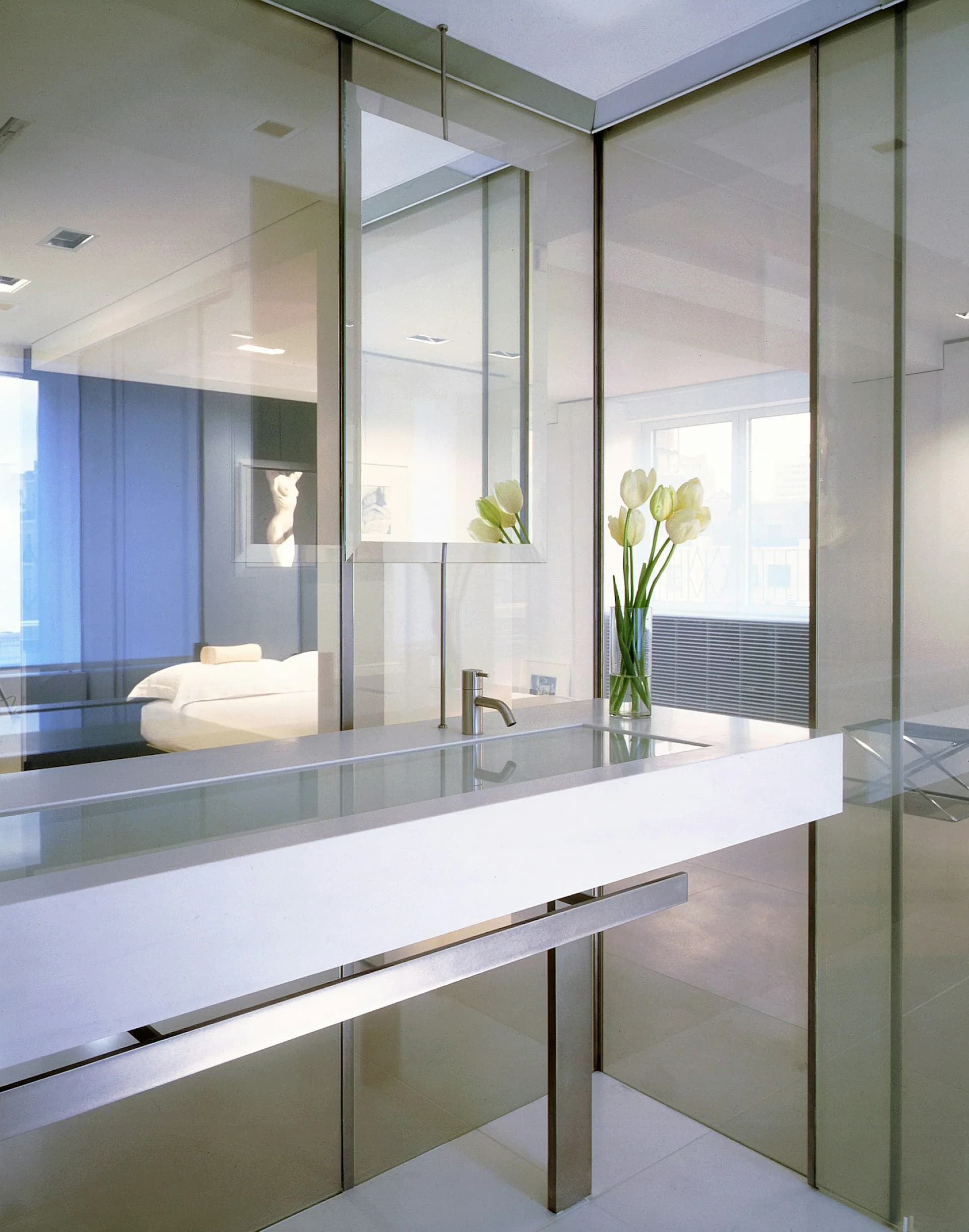 Modern minimalist bathroom with frosted glass partitions, white vanity, and crisp recessed lighting, rendered by Gabellini Sheppard Associates.