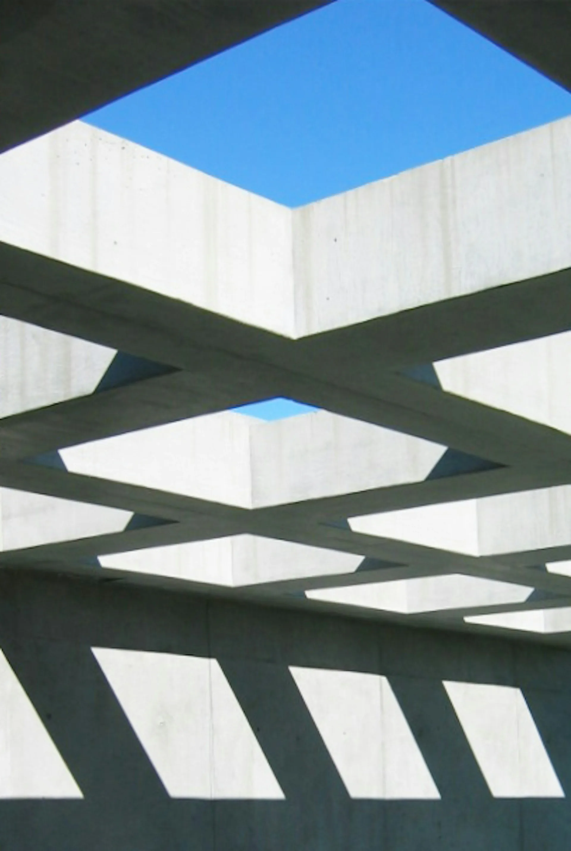 Modern architectural interior featuring white concrete walls with geometric cutouts, dark structural beams creating dramatic shadows, and blue sky visible through skylight openings by Gary Morgenroth Architect, LLC.
