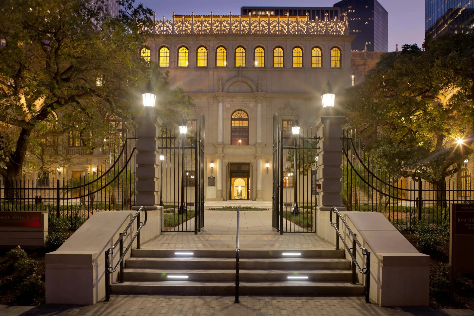 Illuminated neoclassical building facade at dusk with symmetrical entrance, grand staircase, and landscaped courtyard by Gensler.