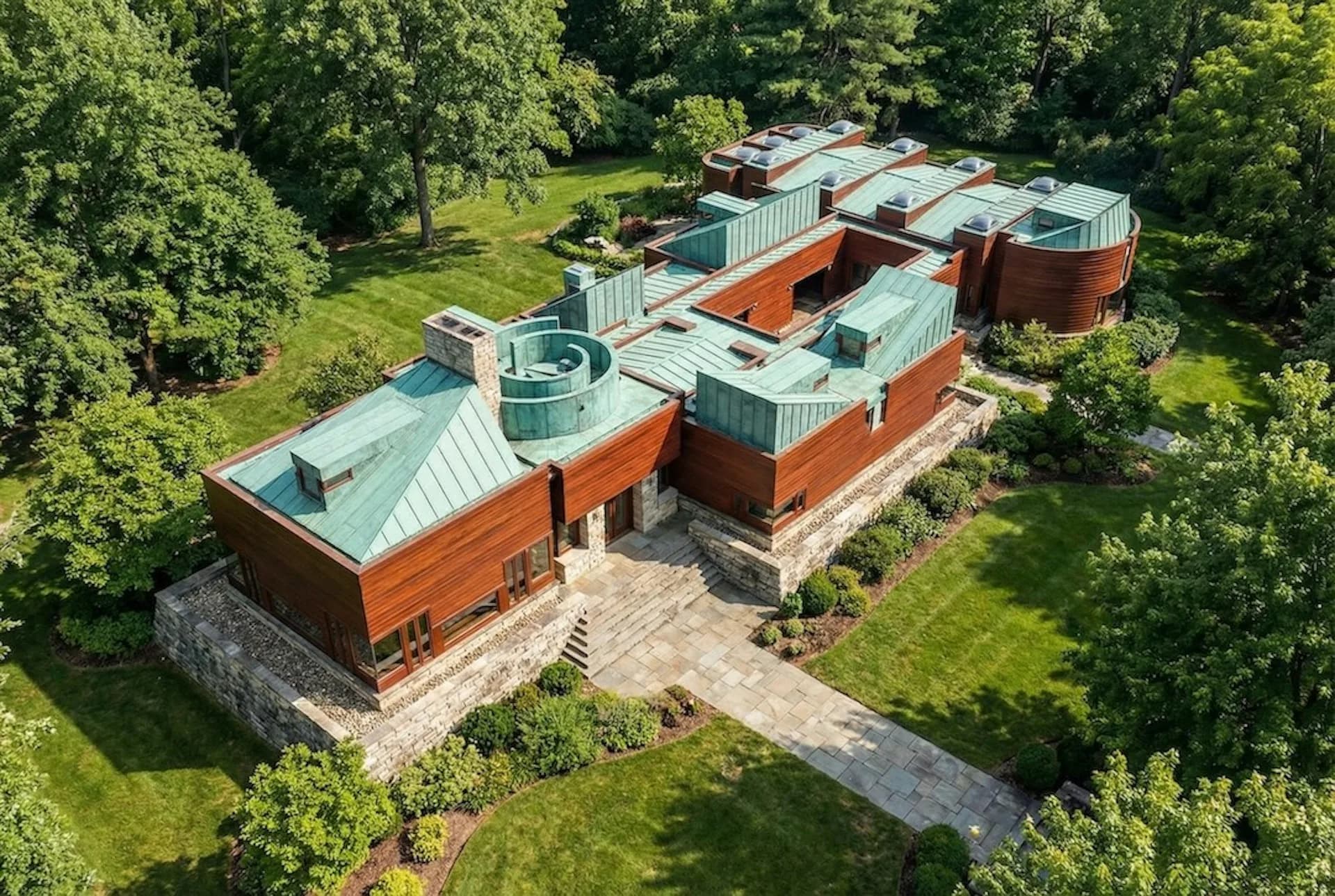 Aerial view of a contemporary residential complex with copper-red brick and green metal-roofed volumes nestled among mature trees, designed by George Ranalli Architect FAIA.