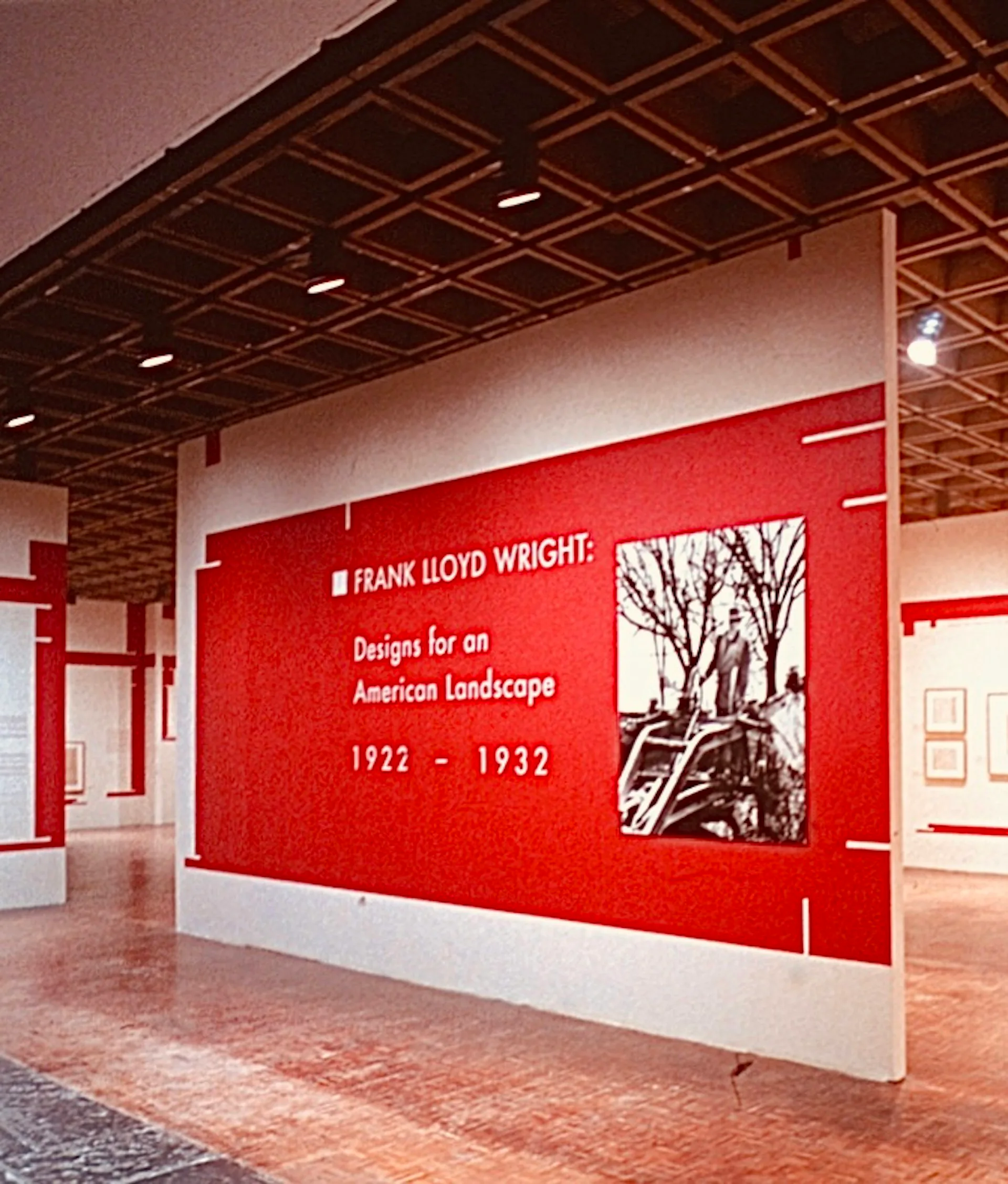 Museum exhibition gallery with bright red accent wall featuring Frank Lloyd Wright text and photography, designed by George Ranalli Architect FAIA.
