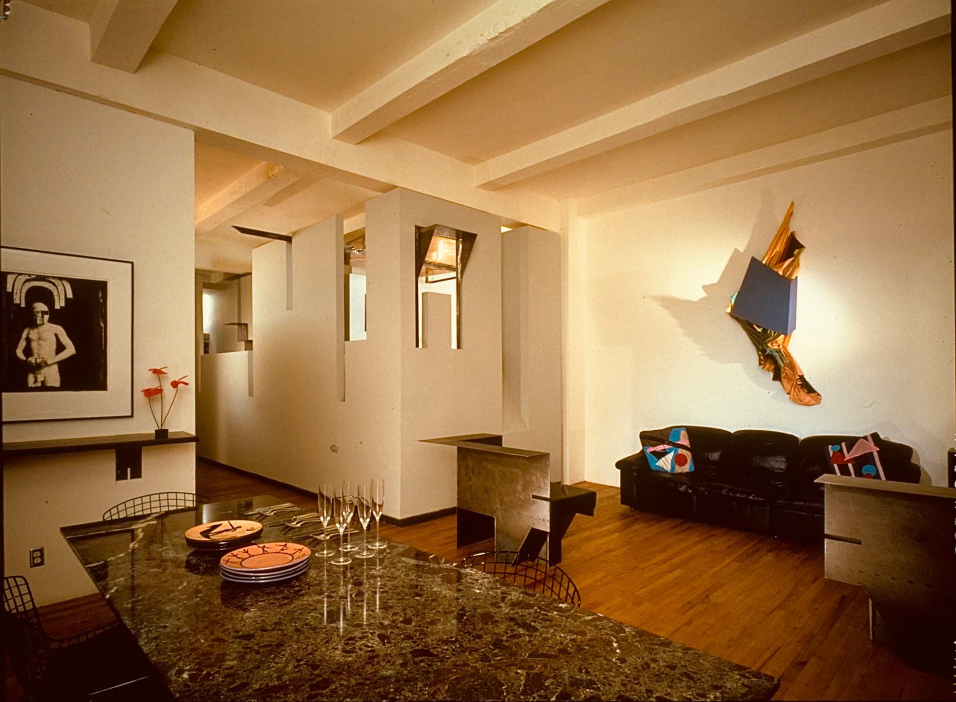 Contemporary open-plan apartment with granite countertop, wooden flooring, dark sofa, and sculptural wall art in warm neutral tones by George Ranalli Architect FAIA.