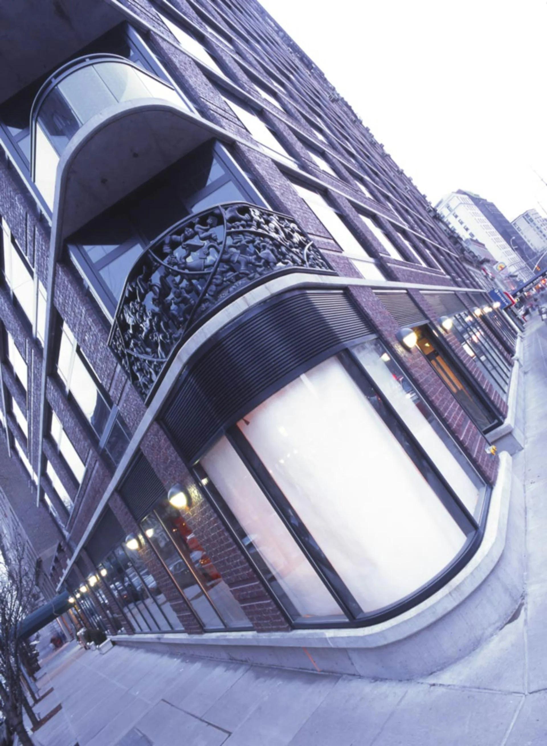 Modern architectural detail of a curved glass storefront with illuminated signage and ornamental metalwork above, showcasing contemporary design by Gerner Kronick + Valcarcel, Architects, DPC.
