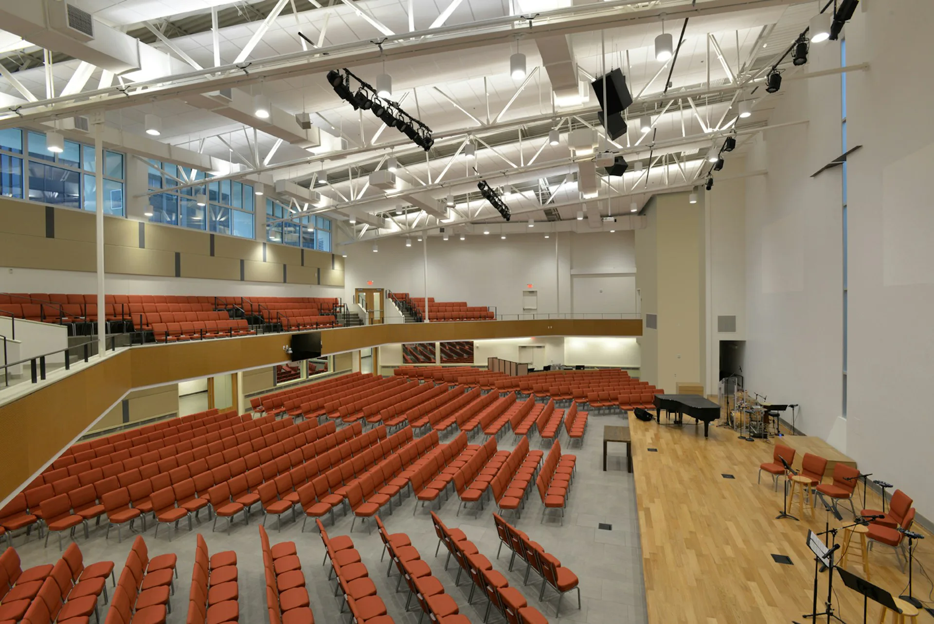 Modern auditorium interior featuring tiered red seating, wood flooring, industrial ceiling with exposed ductwork and theatrical lighting by Gertler & Wente Architects.
