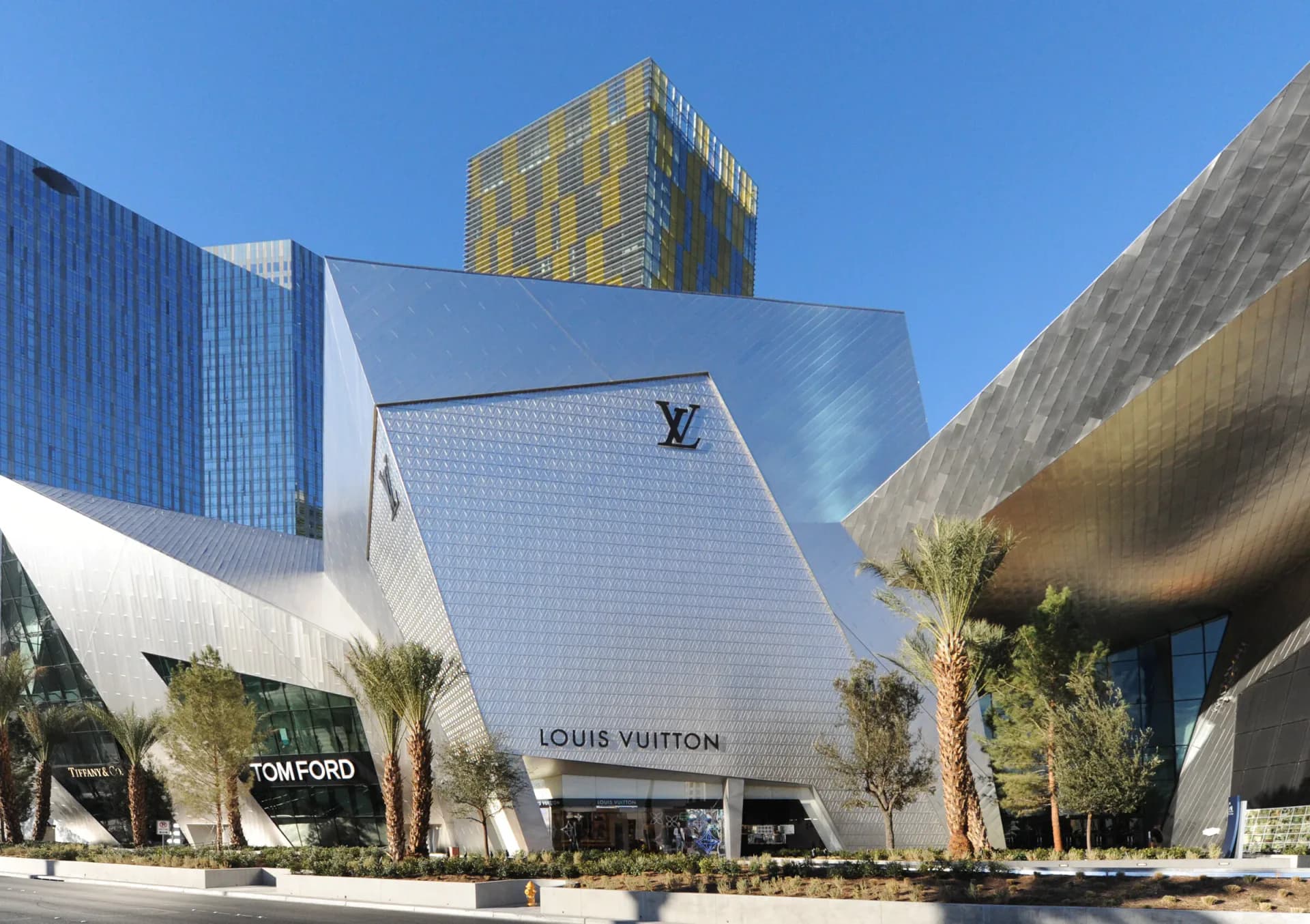 Modern luxury retail building with white geometric facade, curved forms, and integrated landscaping, anchoring a contemporary urban plaza by Gertler & Wente Architects.