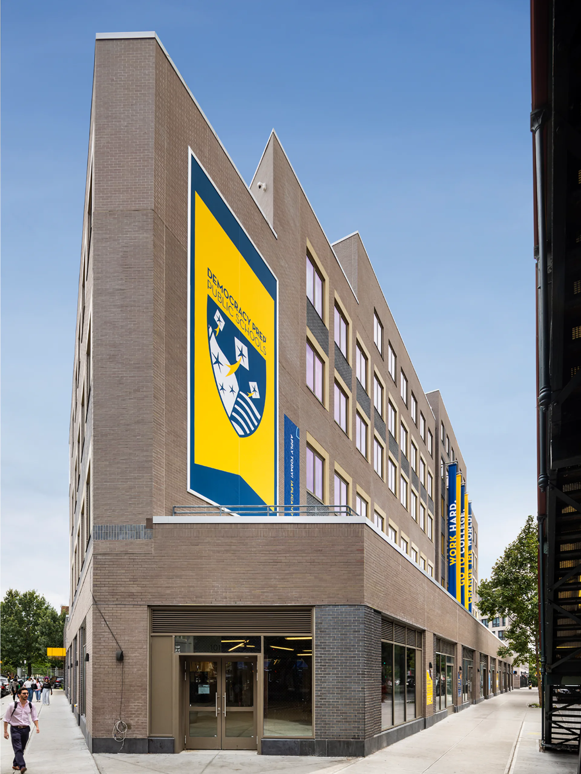Modern brick and concrete residential building with angled roofline and large yellow/blue banner signage on corner facade by GF55 Architects.