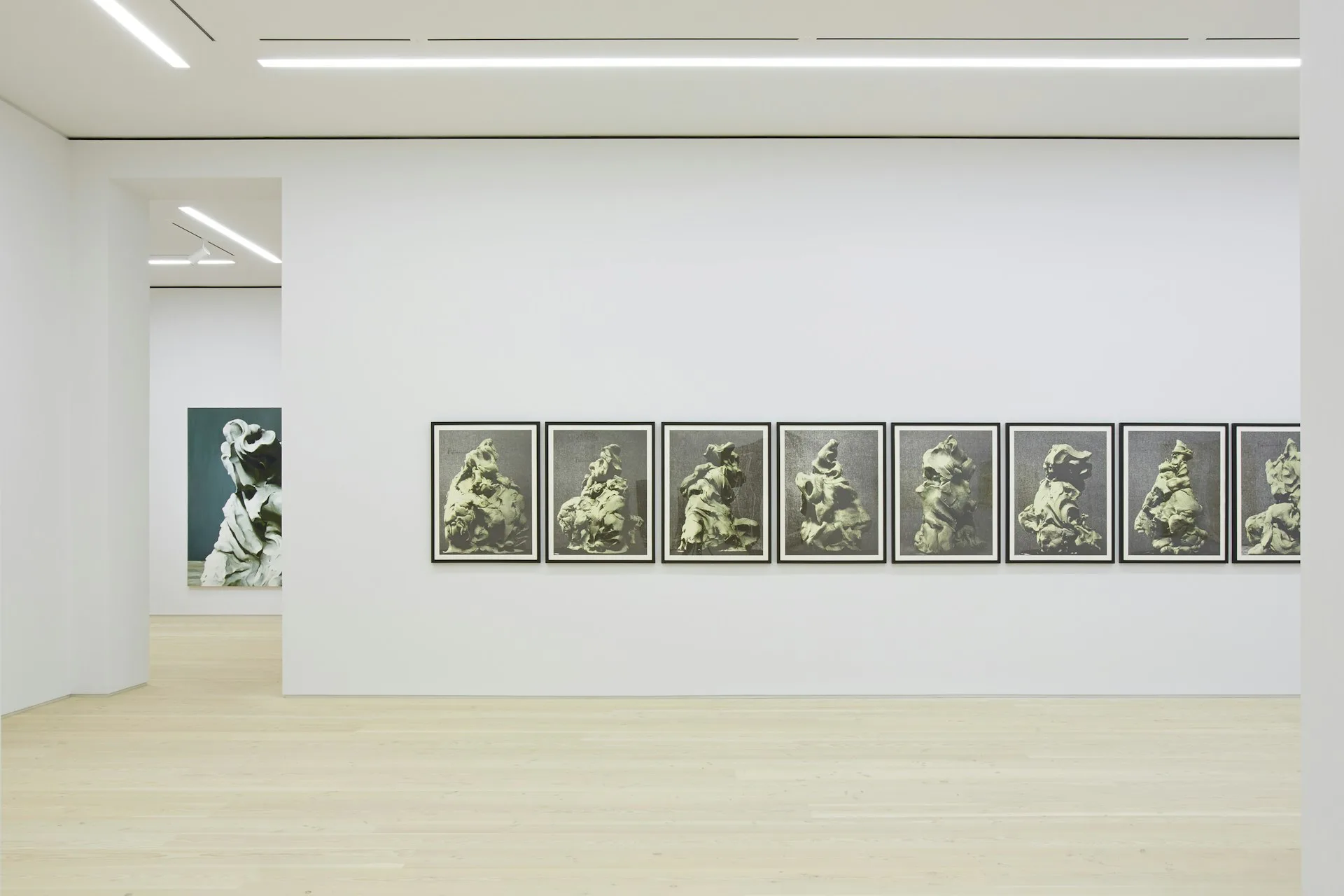 Minimalist gallery space with white walls displaying a series of framed artworks and a single dark panel, polished concrete flooring, and linear ceiling lights by Glickman Schlesinger Architects.