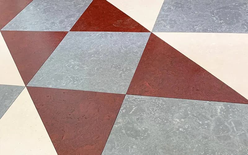 Geometric floor pattern with interlocking triangular tiles in burgundy, grey, blue, and cream tones by Globus Cork.