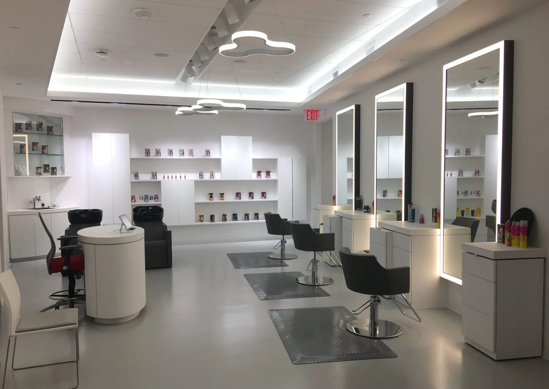 Modern salon interior with white and gray palette, multiple styling stations with black chairs, illuminated mirror cabinets, and polished concrete flooring by Goldstick Studio.