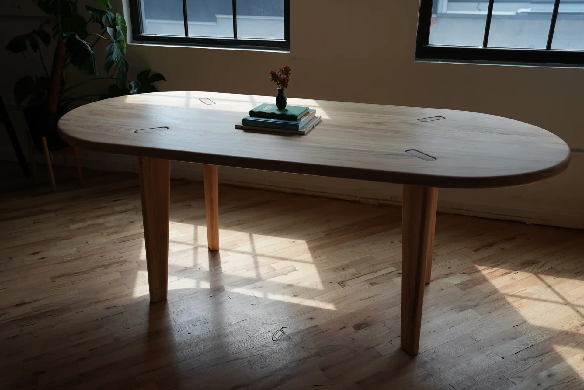 Oval wooden dining table with tapered legs and marble top in a sunlit room with hardwood flooring, designed by Good Chair Co.