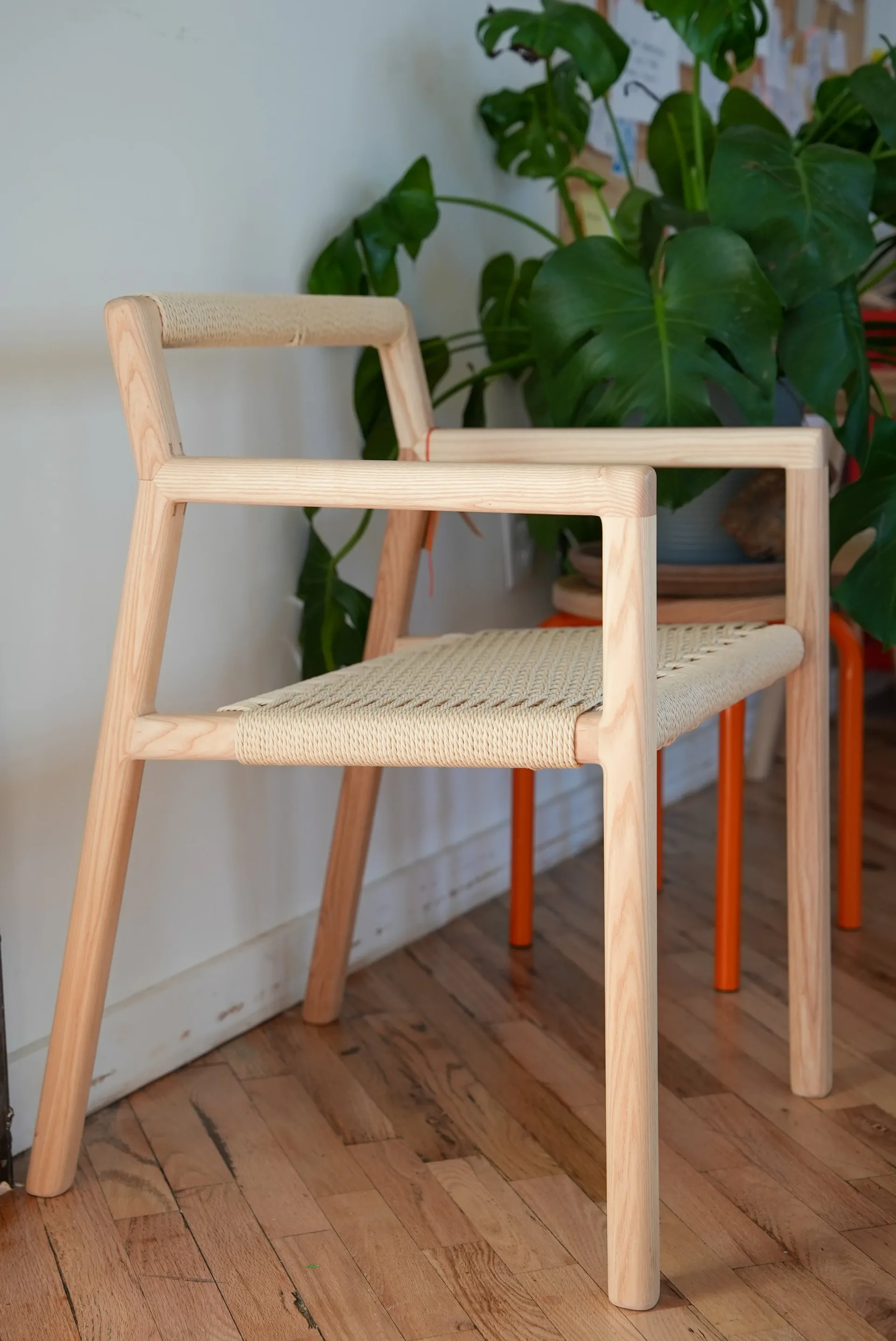 Light wood frame chair with woven seat and backrest, positioned in bright interior space with potted plant and wooden flooring by Good Chair Co.