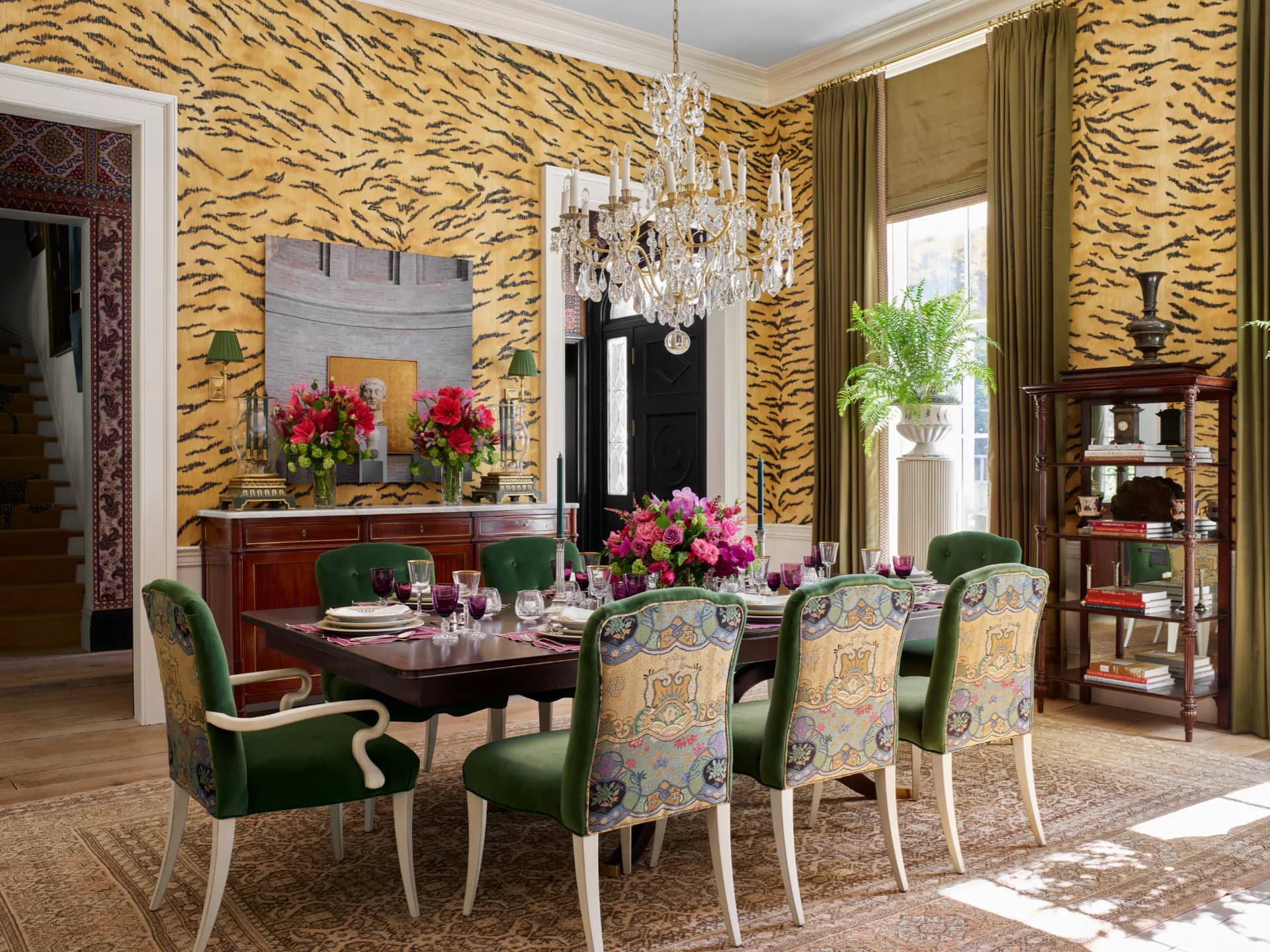 Formal dining room with gold tiger-stripe wallpaper, dark wood table, upholstered chairs, crystal chandelier, and floral arrangements by Gracie.