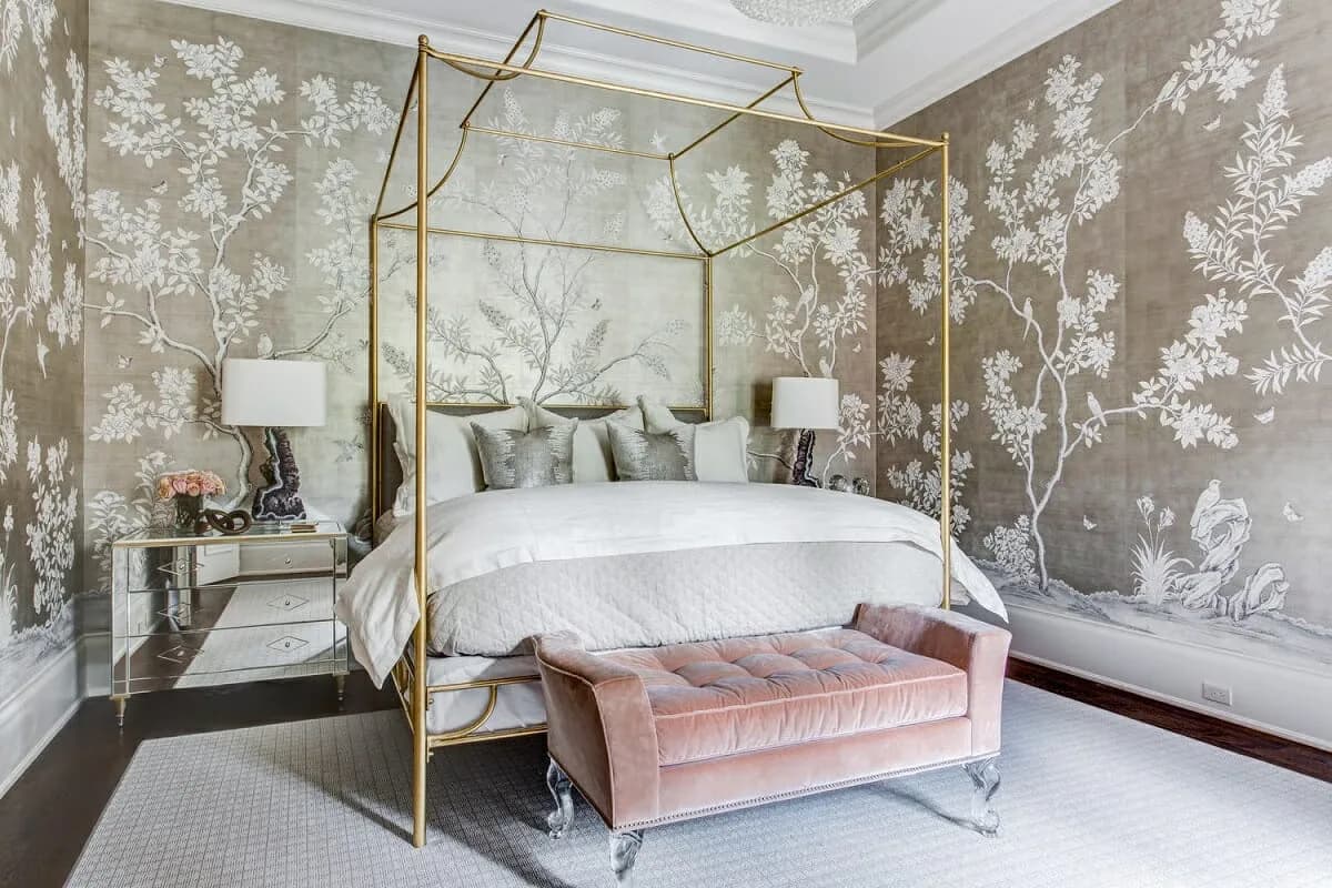 Luxurious bedroom with brass canopy bed, taupe chinoiserie wallpaper, marble nightstands, and pink velvet bench by Gracie.