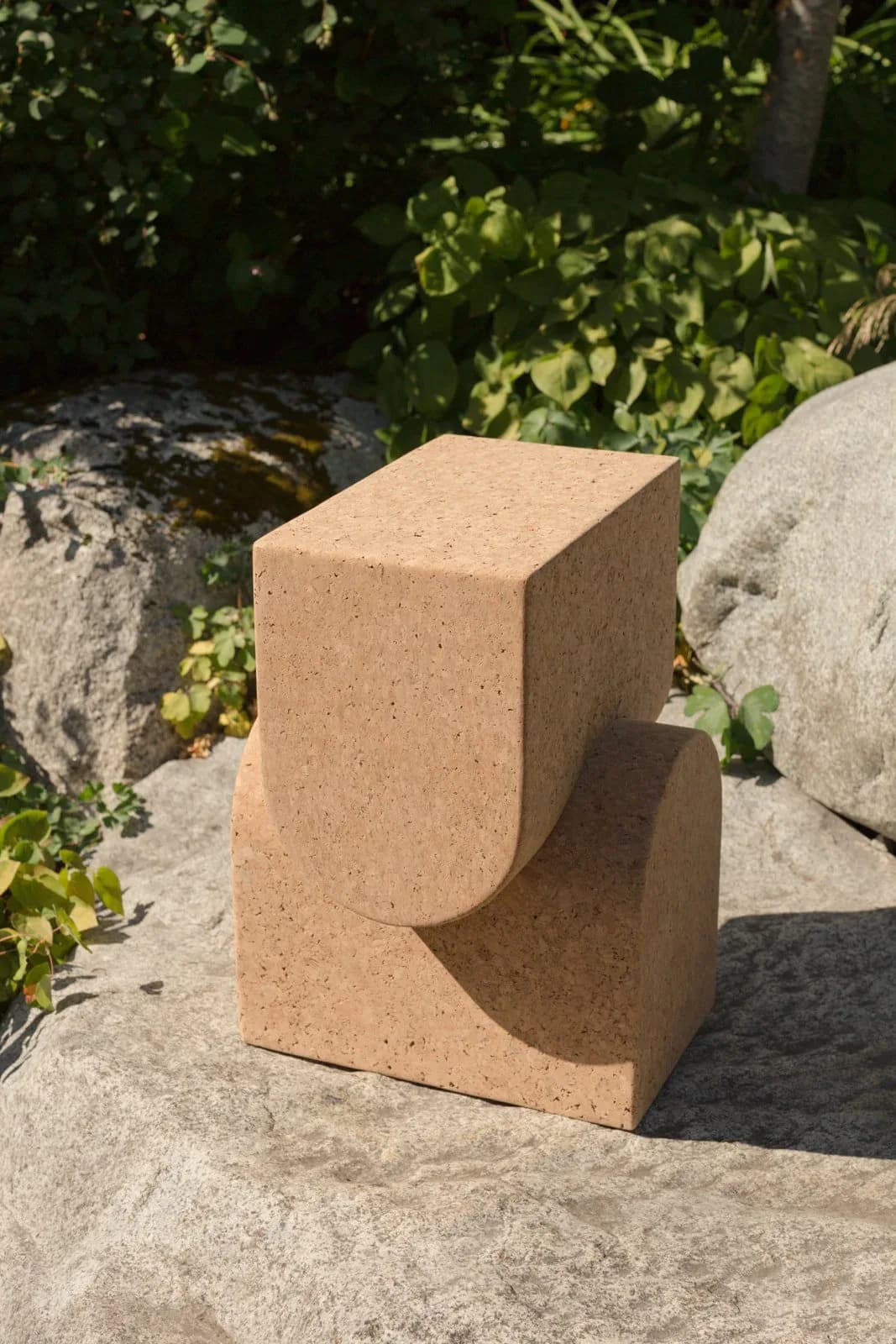 Terracotta sculptural object with curved cutout detail sits on stone surface surrounded by boulders and greenery by Grain Design.