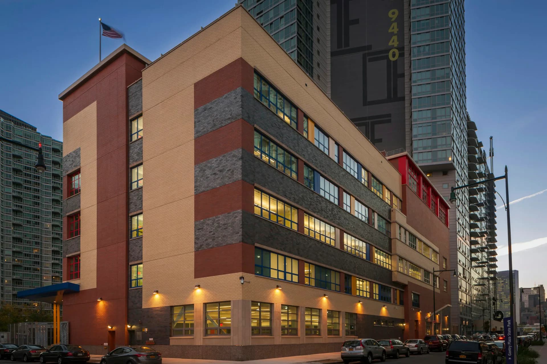 Contemporary mixed-use building with terracotta and gray striped facade, illuminated ground-floor retail spaces, and tall residential towers beyond, designed by Gran Kriegel Associates Architects and Planners.